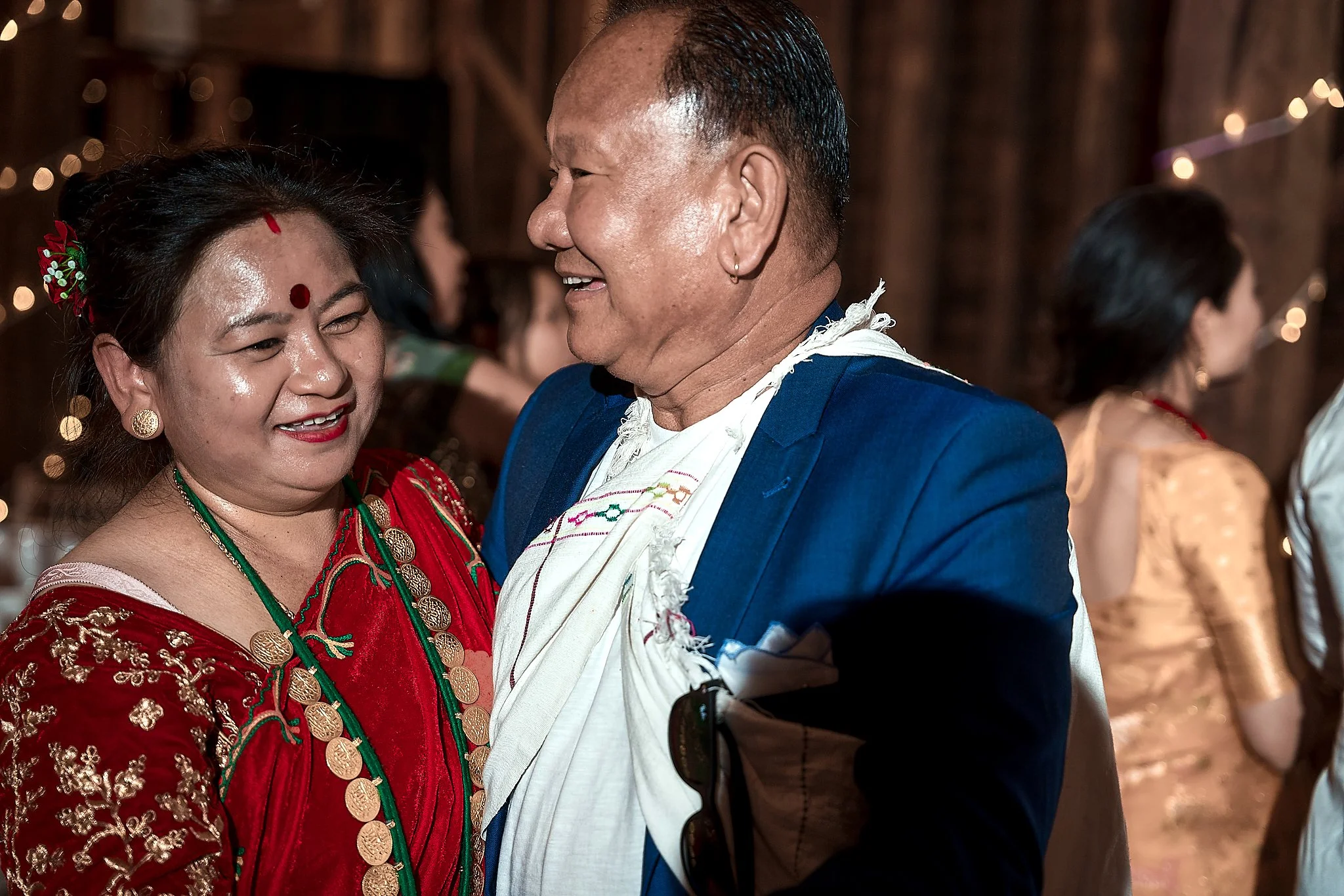 Two people, a woman and a man, smiling and looking at each other, dressed in traditional Nepali attire at a festive event.