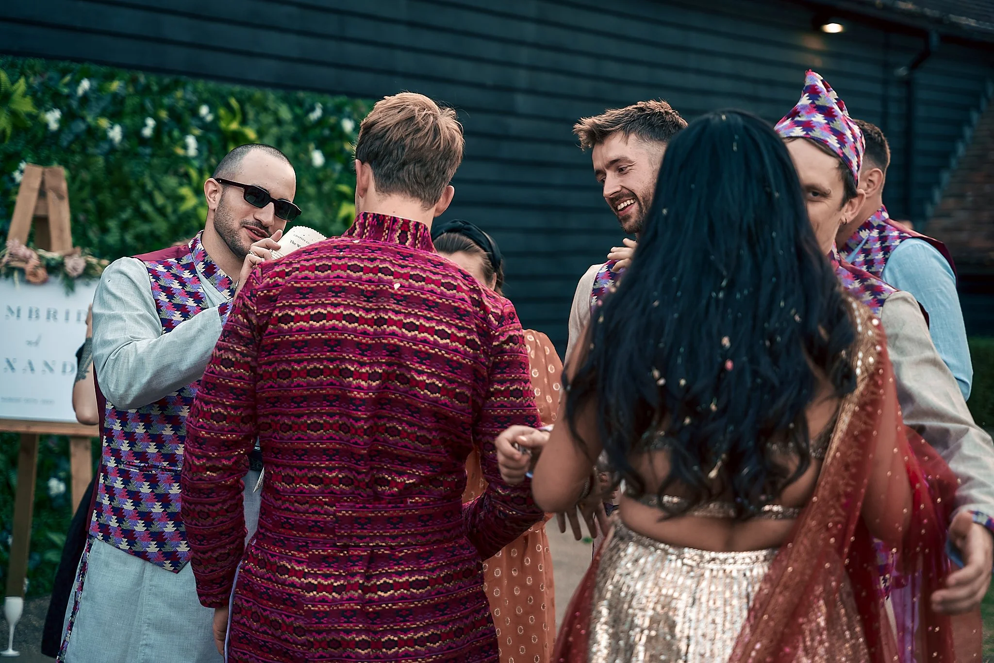 A group of people at a wedding celebration, dressed in traditional South Asian attire, standing together and smiling.