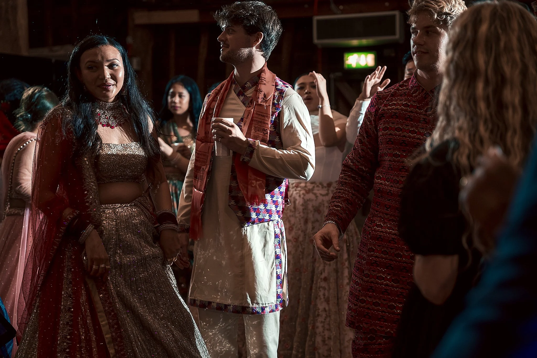 Group of people dancing and socializing at a party or celebration, wearing fashionable and colorful traditional outfits.