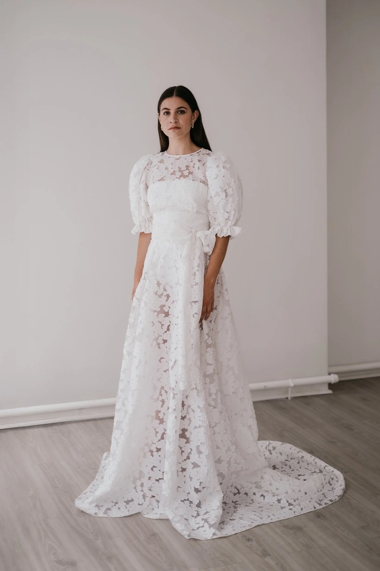 A woman standing against a plain background wearing a textured bridal skirt and matching top by British bridal designer Unbridled studio.