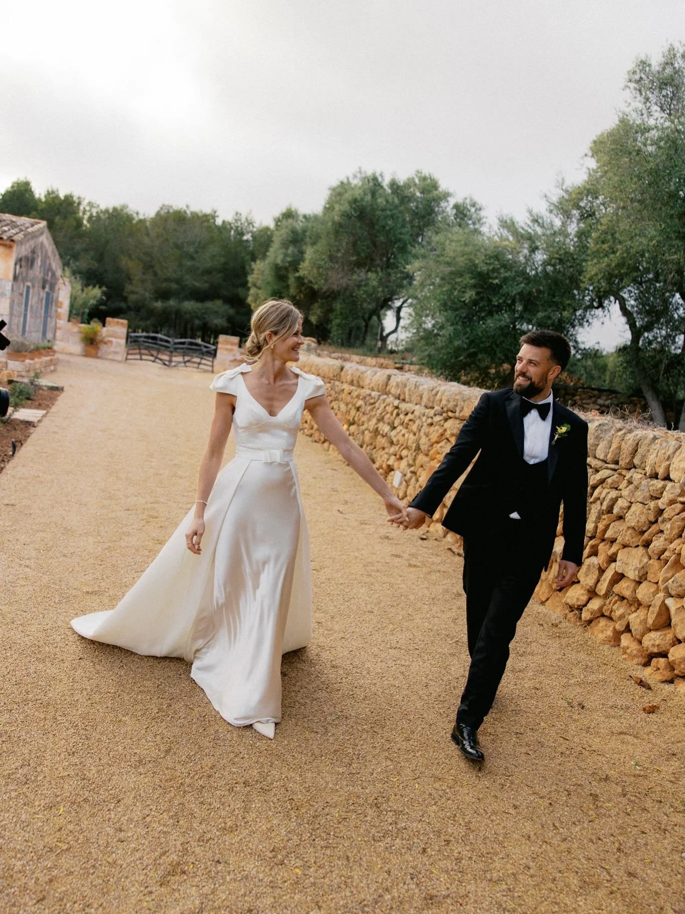 We have been SO looking forward to a peek of Amy and Alex&rsquo;s wedding in sunny Mallorca. Amy wore a bias cut silk satin gown with sculptural cap sleeves and double satin overskirt that layered over to create a dramatic train. The look was accente