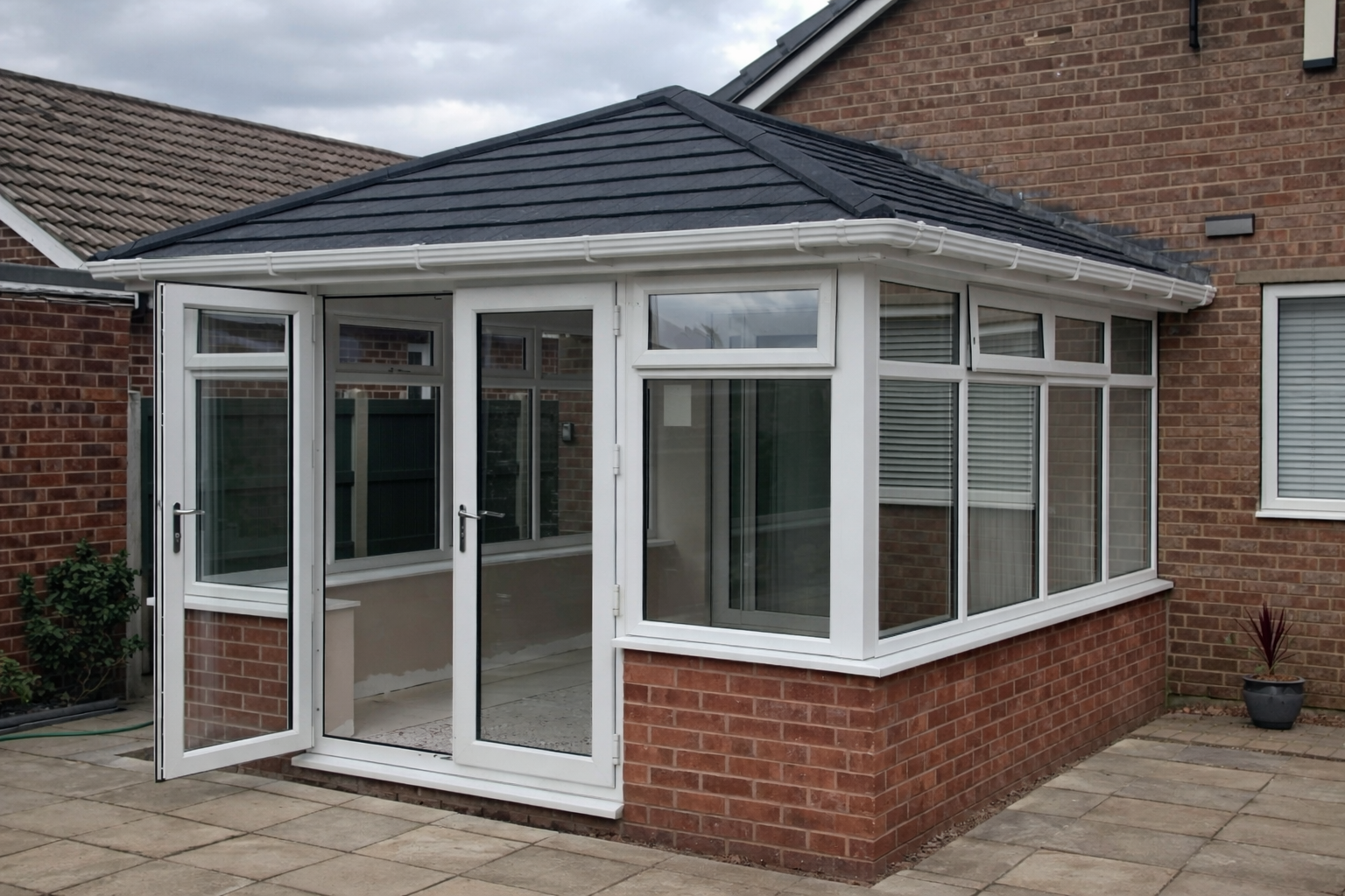 Backyard patio with a brick building, featuring a glass-enclosed porch with white trim and large windows, a small plant in a pot, and stone paving paving.