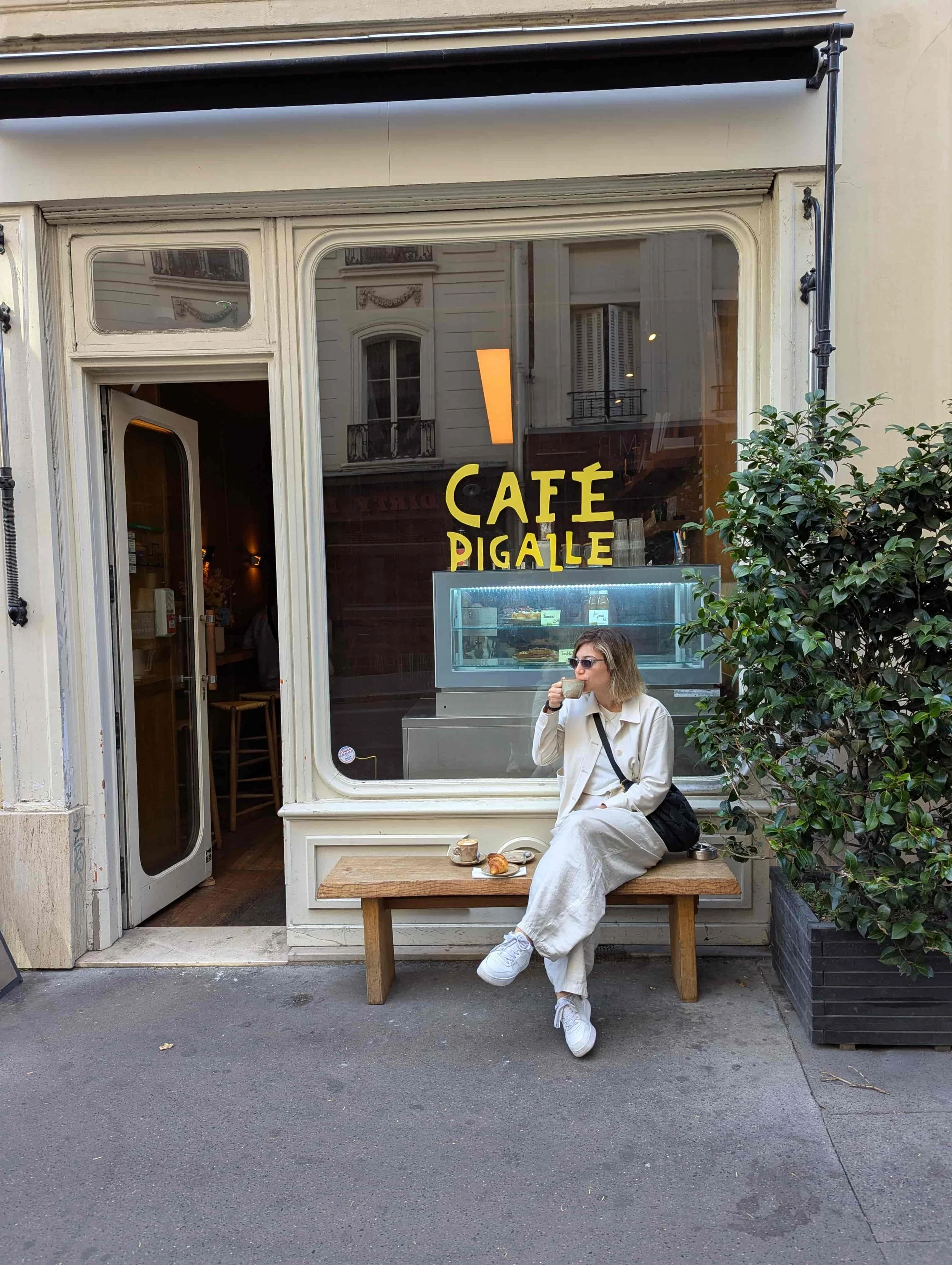 A woman sitting on a bench in front of a cafe in Paris drinking coffee