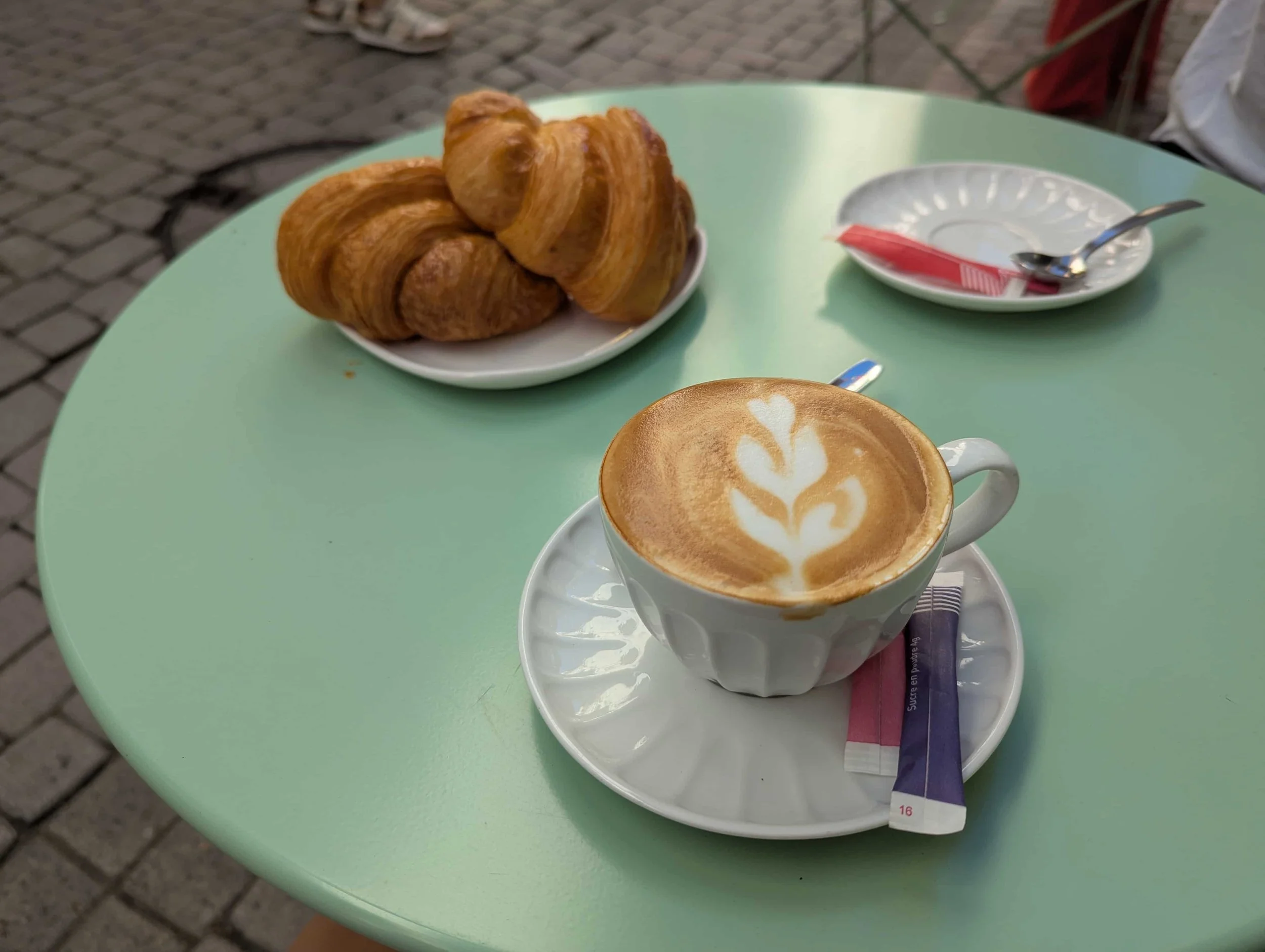 A green table with a Flat white and two croissants