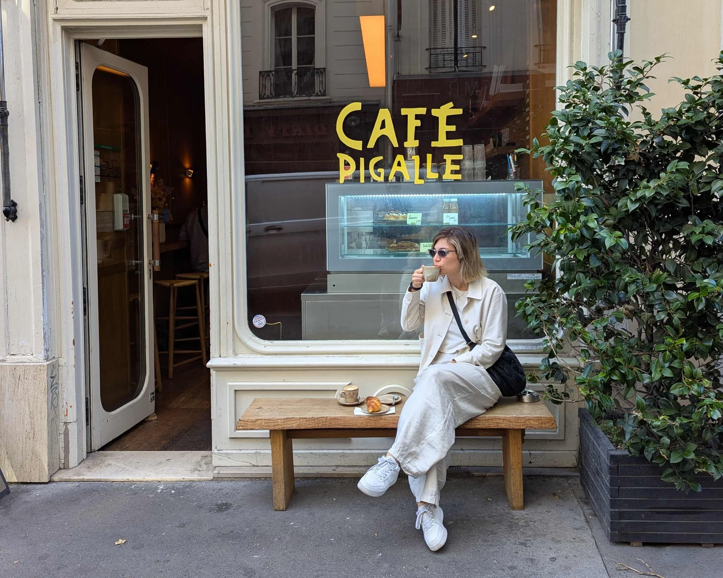 A woman sitting in front of a cafe drinking coffee