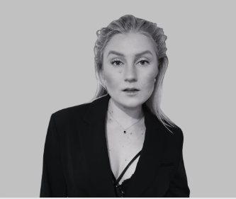 Black and white portrait of a woman with shoulder-length wavy hair, wearing a dark blazer, smiling at the camera.