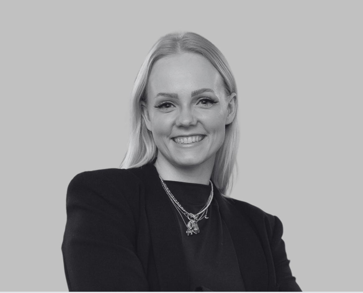 Black-and-white portrait of a woman with shoulder-length hair, smiling, wearing a dark blazer, against a plain background.