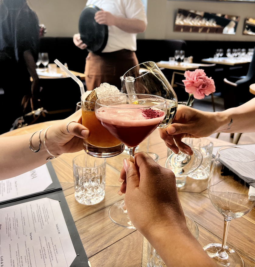 Kolme ihmistä nostavat erilaisia juomia lasiin ylintä juhlajuomaa, joka näyttää olevan punainen ja koristeellinen.