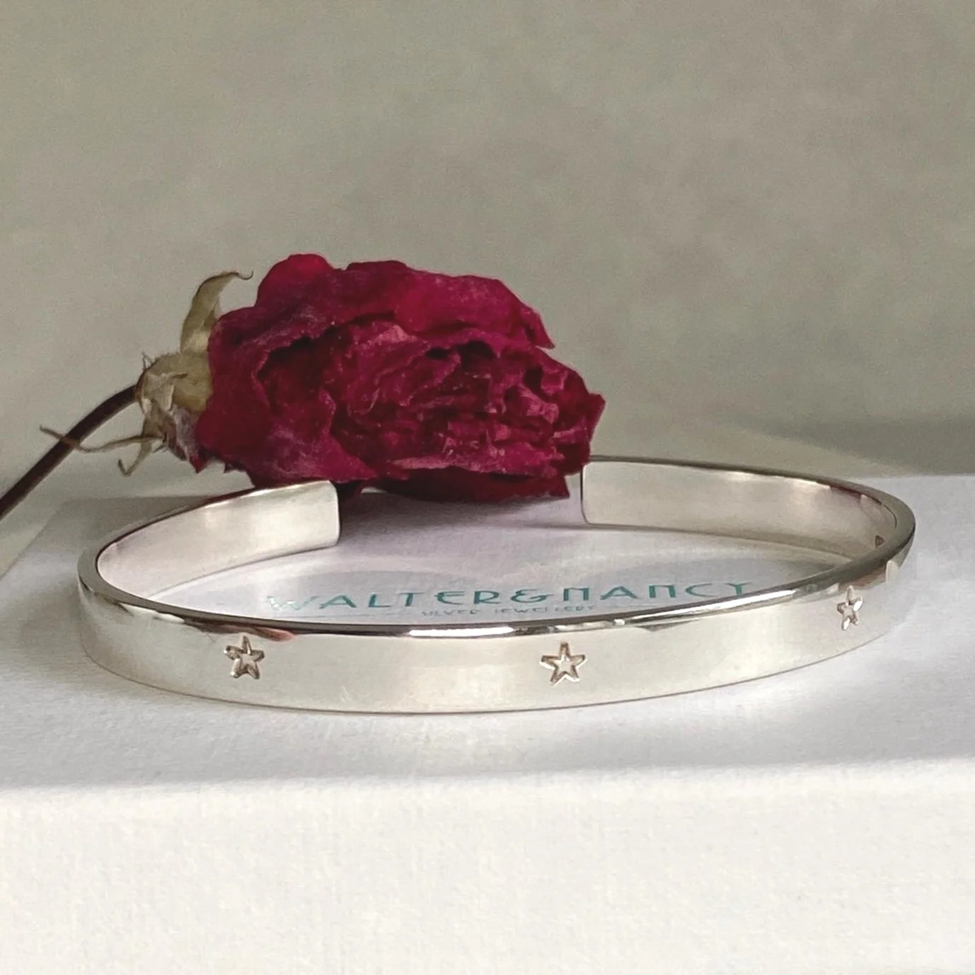 Sterling silver, hand made star cuff bangle sitting in front of a red rose.