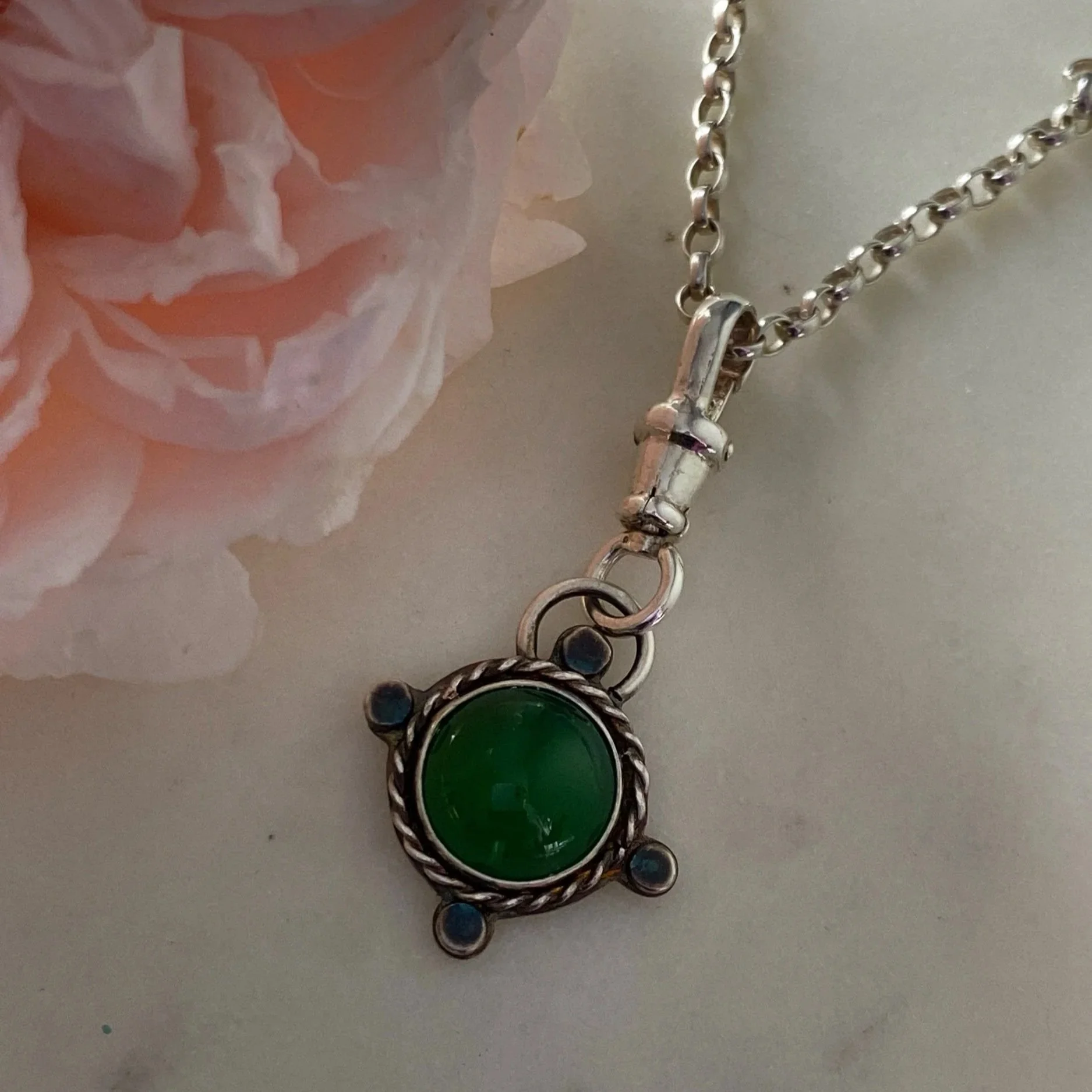 Walter and Nancy Jewellery's handmade, sterling silver and green onyx necklace charm sitting beside a light pink rose.