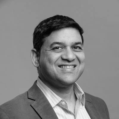A portrait of a woman with short black hair, wearing a navy blue top, smiling against a gray background.