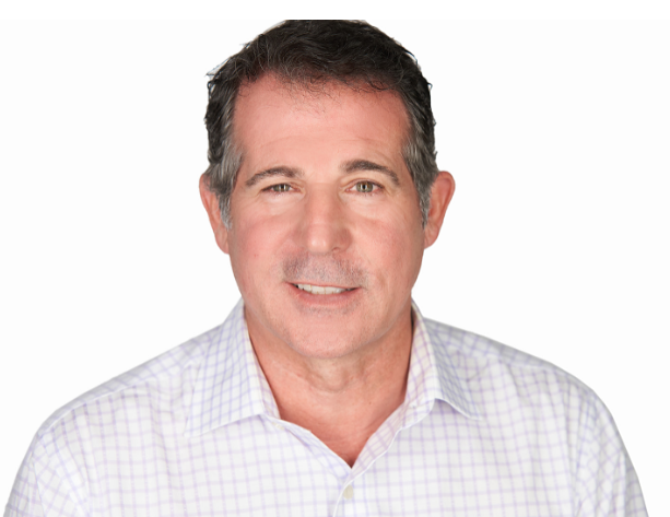 A middle-aged man with short dark hair, light skin, wearing a light checkered shirt, smiling at the camera against a white background.