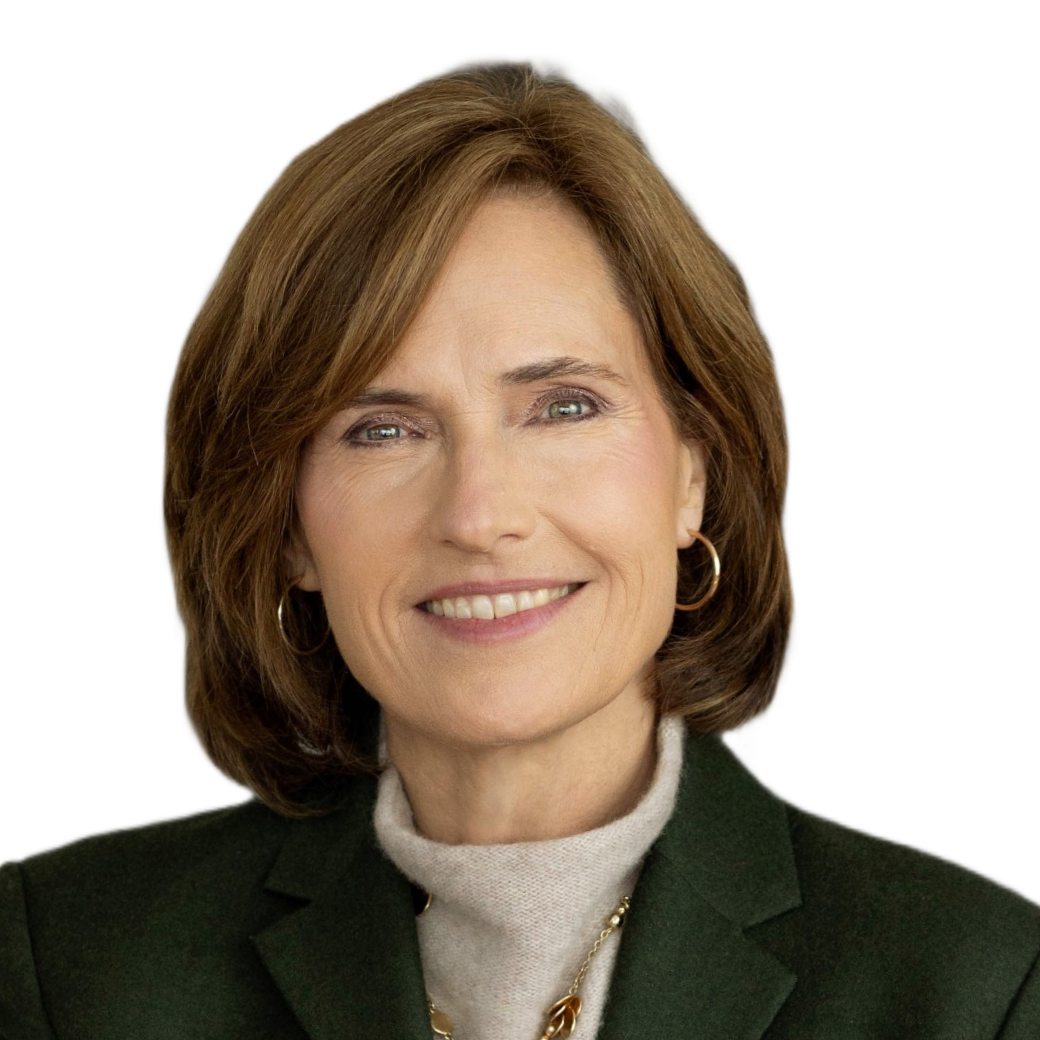 A woman with shoulder-length brown hair, wearing a dark blazer, light-colored turtleneck, and gold jewelry, smiling against a black background.
