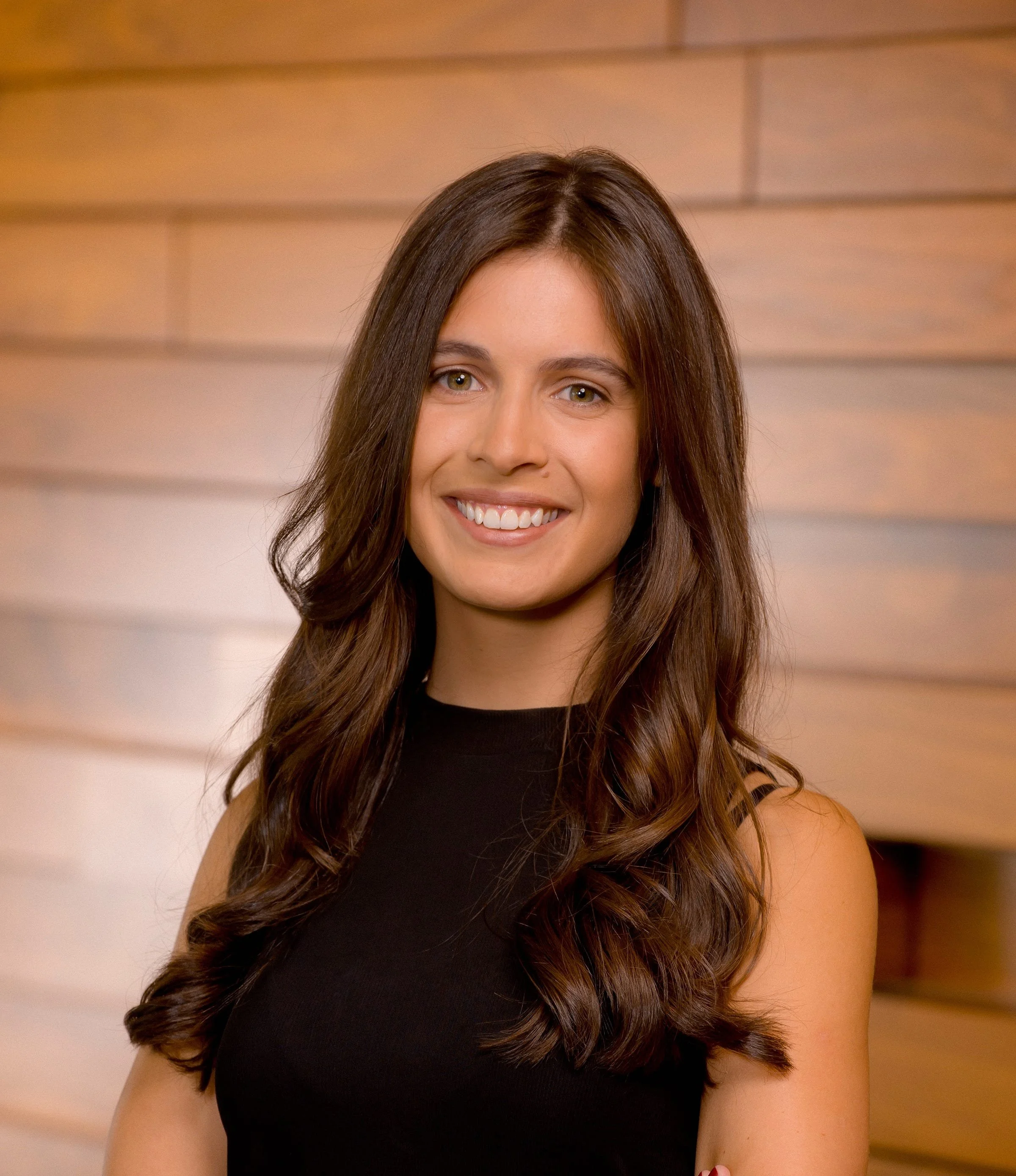 Professional man wearing a dark suit and light blue checkered shirt, smiling at the camera against a gray background.