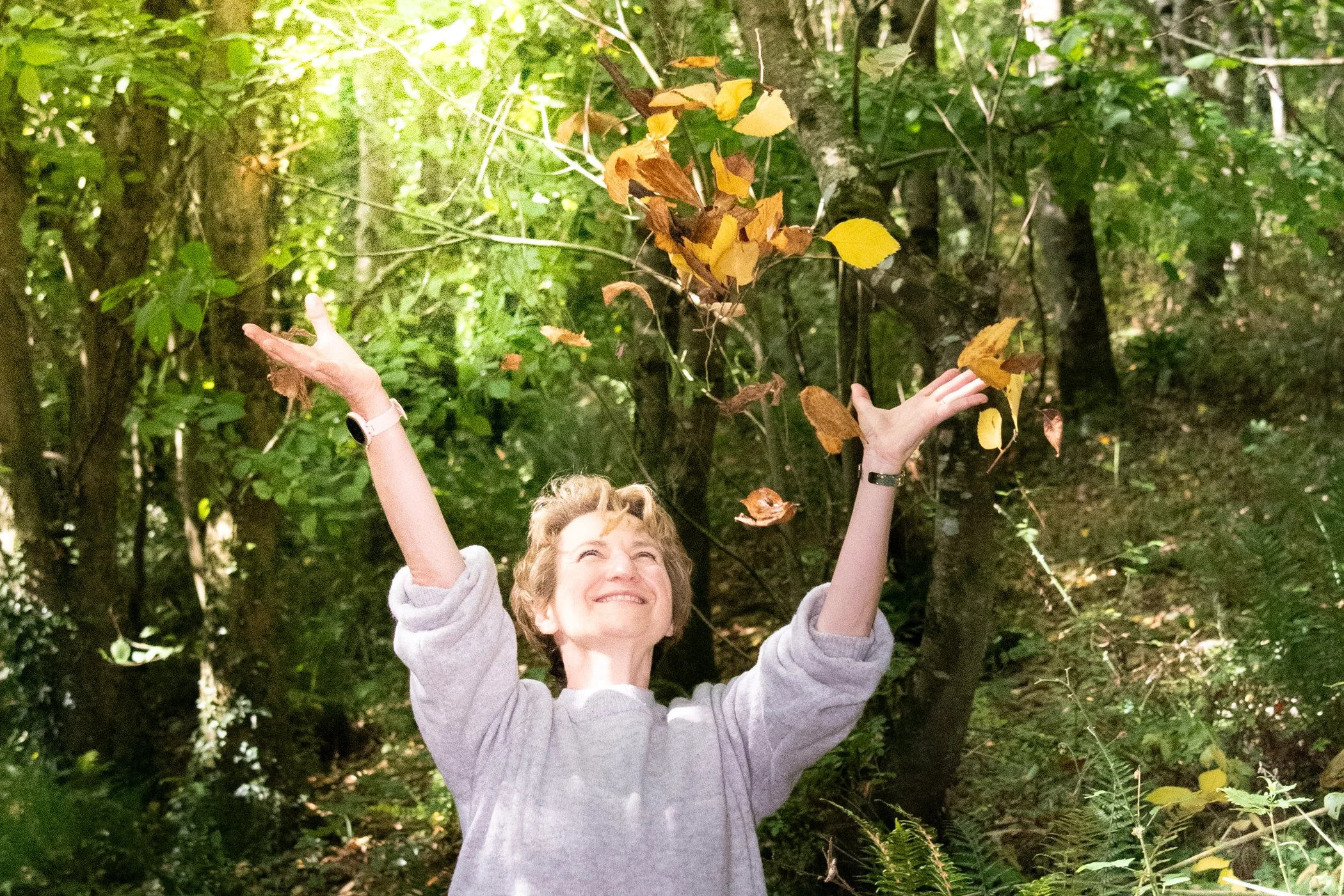 Sandra Dumas Health coach, smiling and throwing some leaves in the air