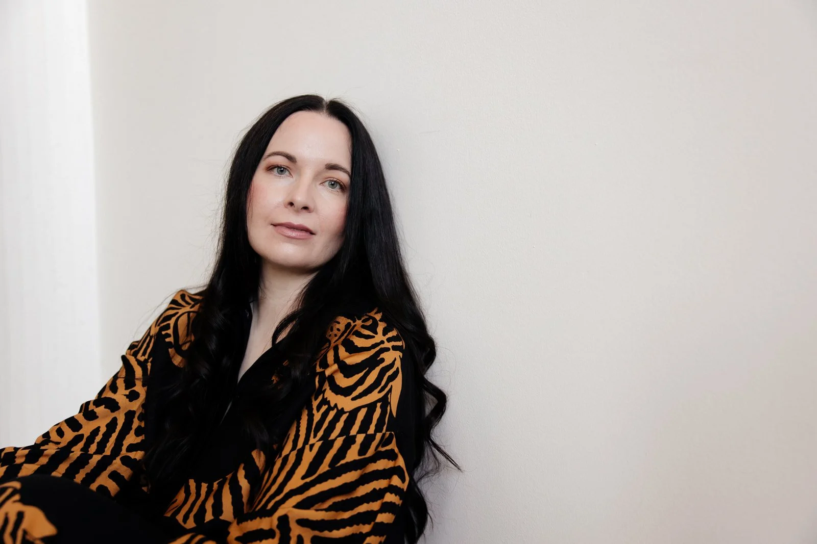 Sara Moon sitting against a plain white wall, wearing a black and orange tiger-striped shirt.
