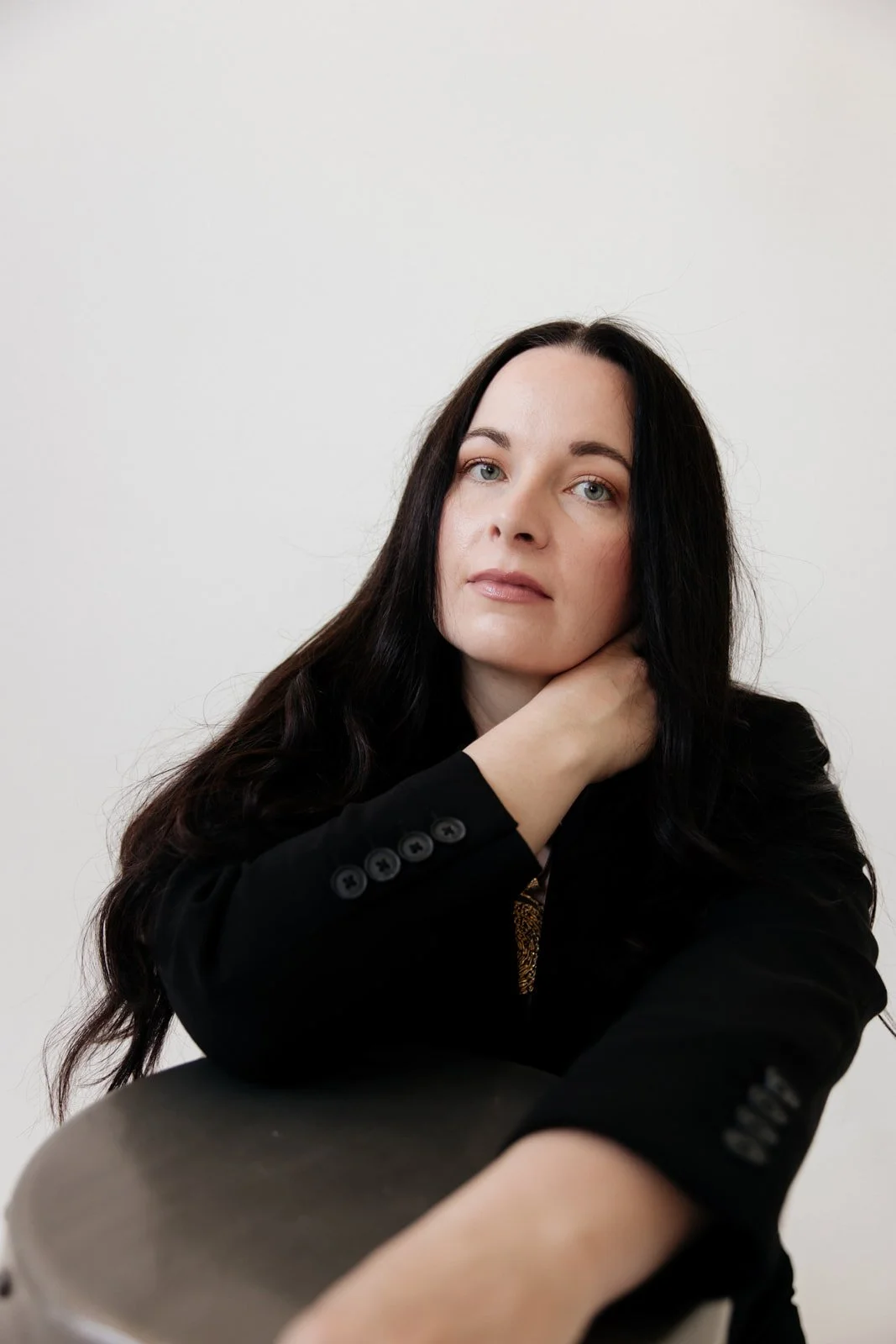 Portrait of Sara Moon wearing a black blazer, resting her head on her hand against a plain white background.