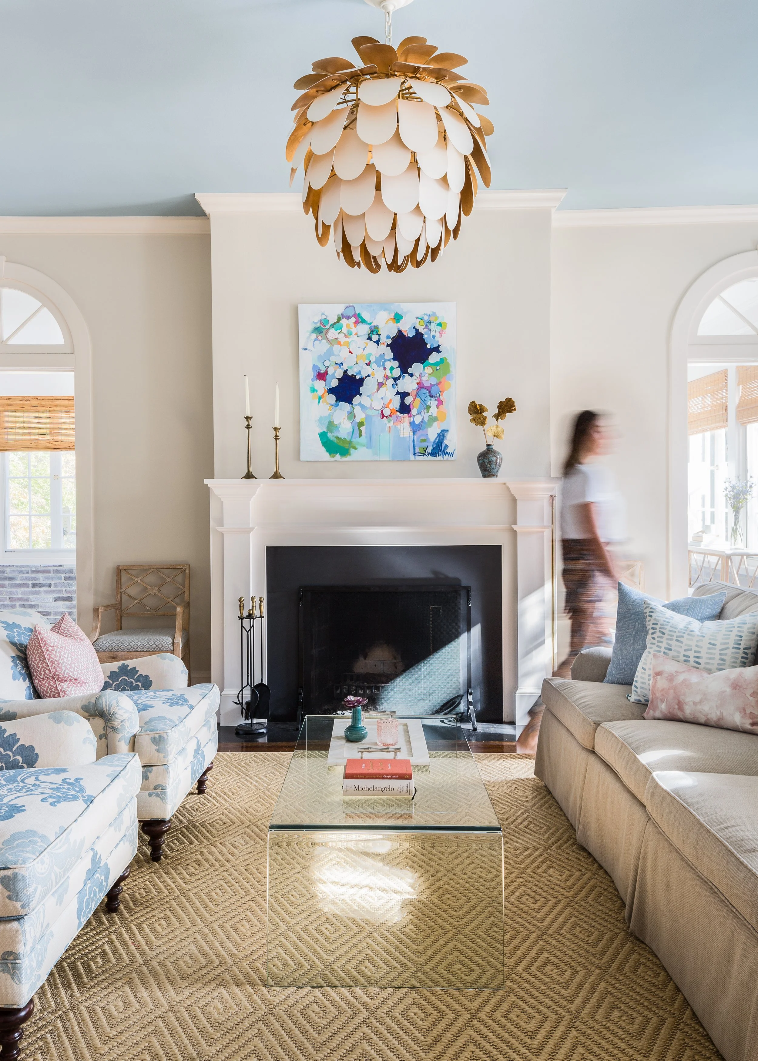 Polished Georgian living room with sofas, a glass coffee table, textured rug, white fireplace, abstract artwork, and a modern chandelier.