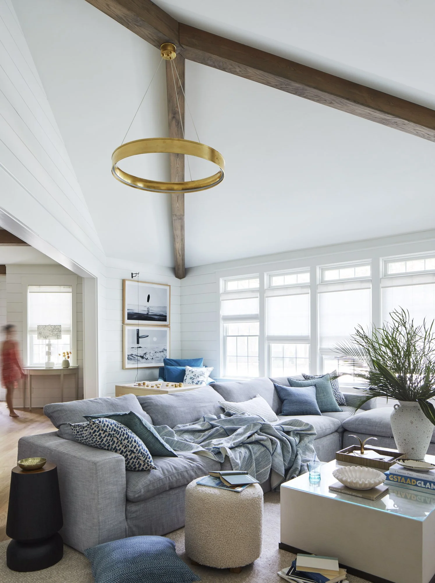Relaxed Rehoboth Beach living room with a large gray sectional, blue-and-white pillows, exposed wood beams, and a circular chandelier.
