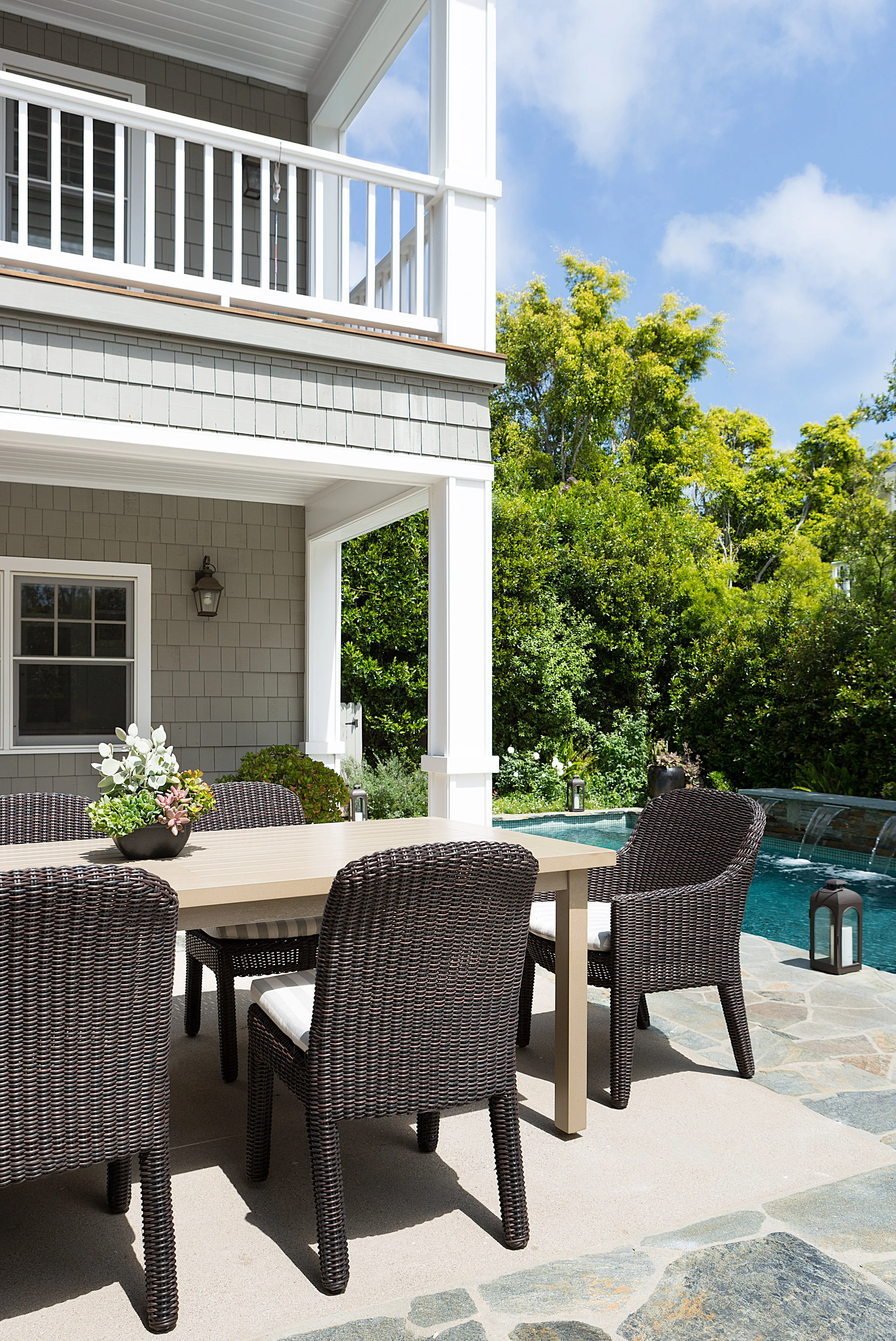 Pacific Palisades backyard with a swimming pool, wicker seating, wood dining table, potted plants, and a gray two-story home.