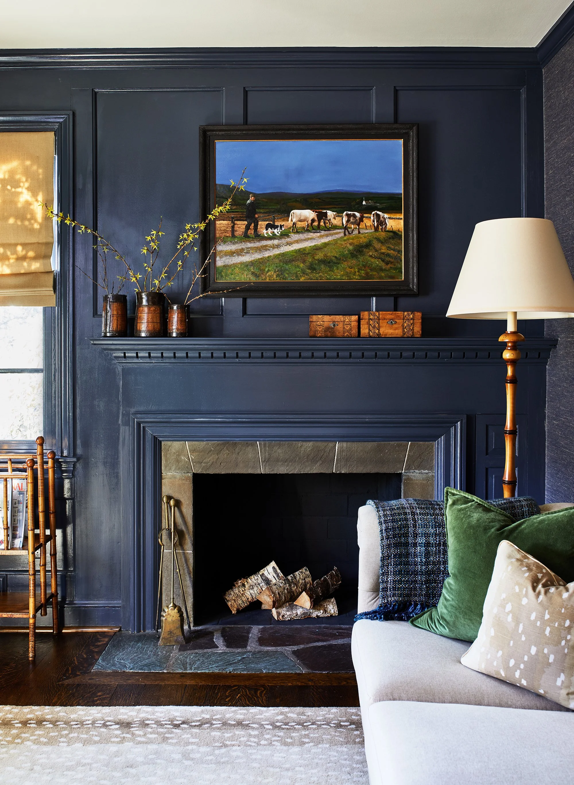 Cozy living room with dark blue wall paneling, a fireplace, framed artwork, sofa with green and beige pillows, and a floor lamp.