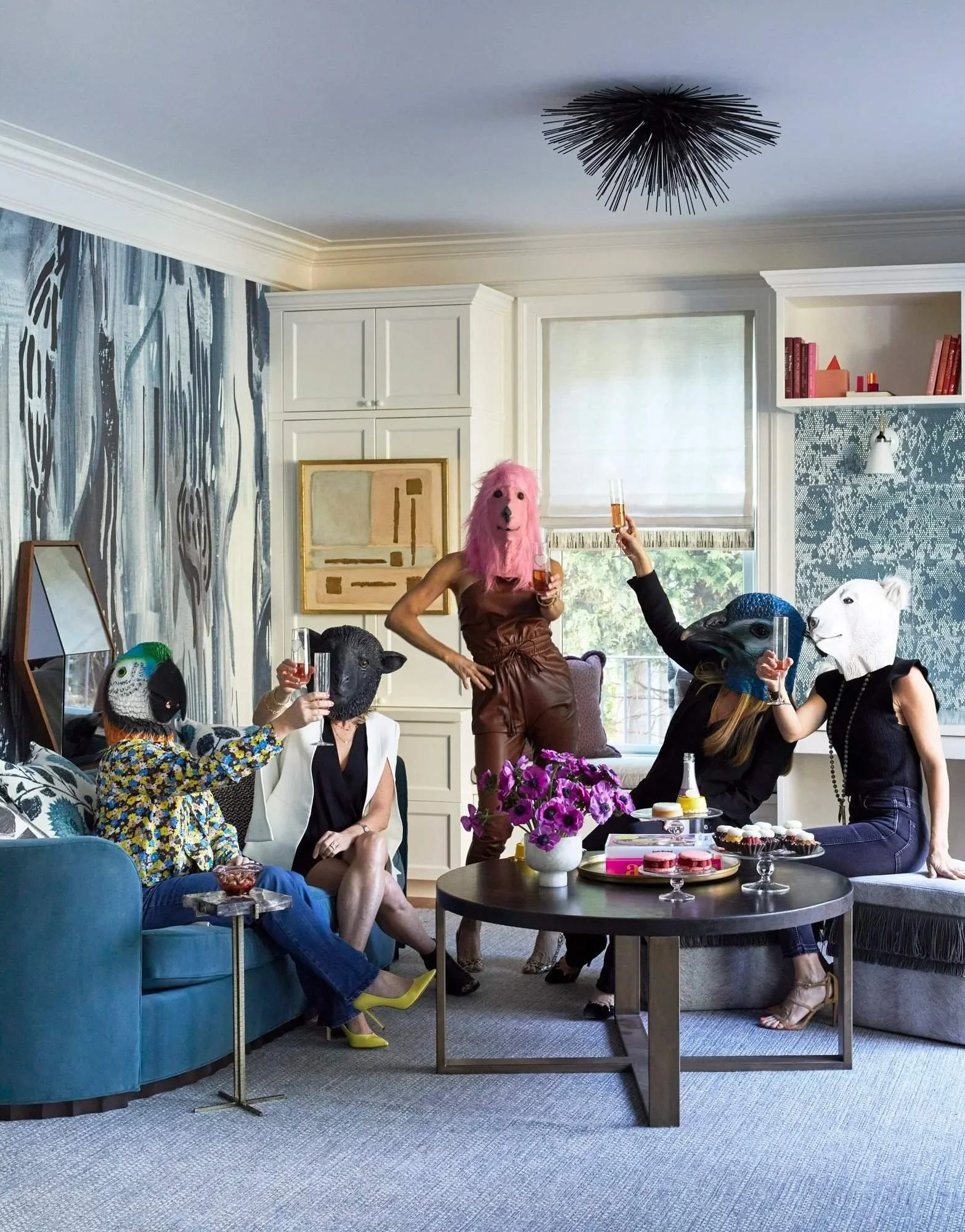 Five women wearing playful animal masks toast together in a layered living room designed for gathering and celebration.