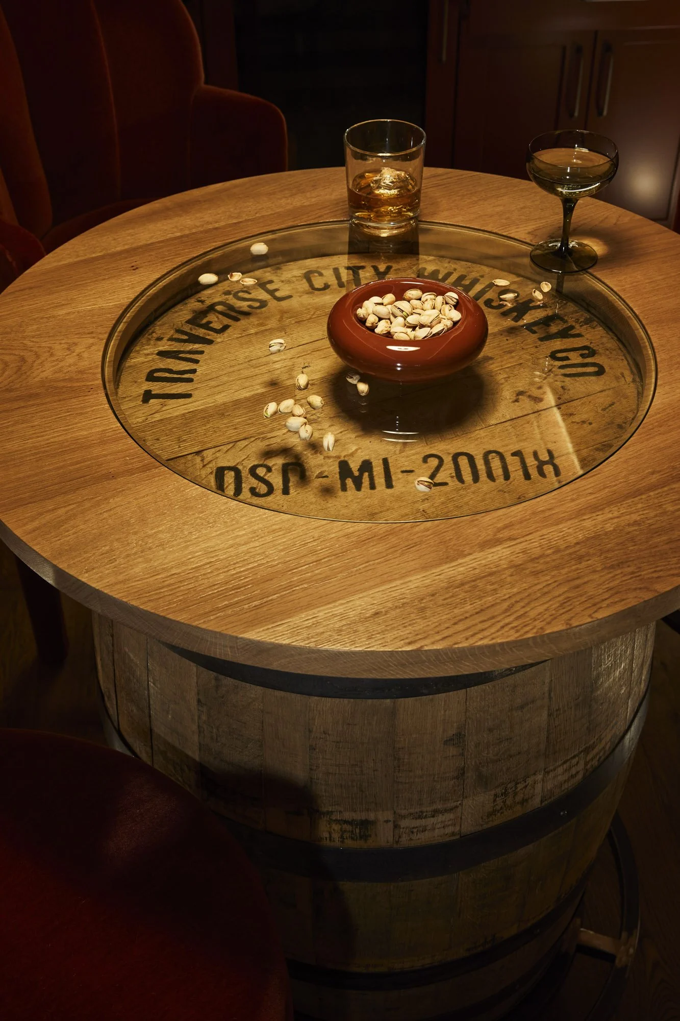 Glass-topped whiskey barrel table holding two drinks and a bowl of pistachios in the hidden speakeasy.