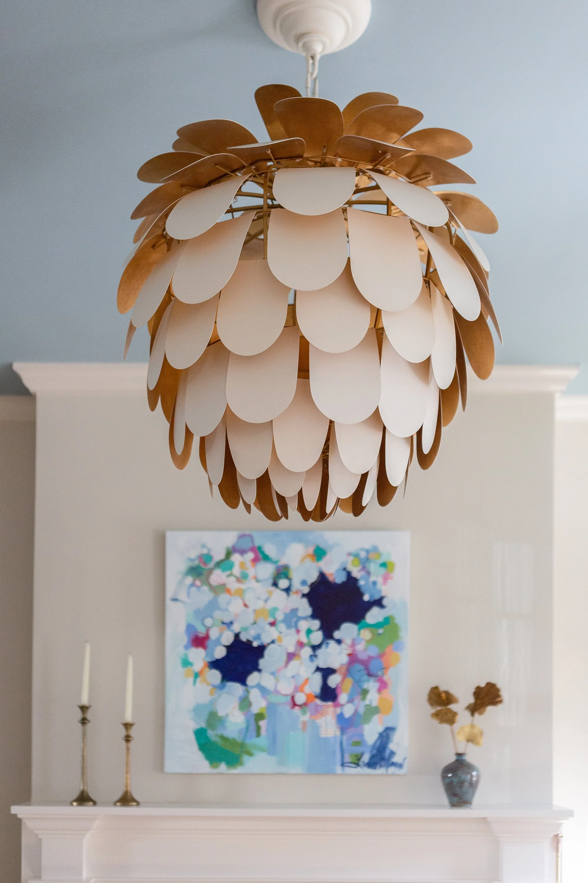 Formal living room with a beige sofa, floral armchairs, glass coffee table, white fireplace, abstract artwork, and Sculptural chandelier with overlapping petal-like forms