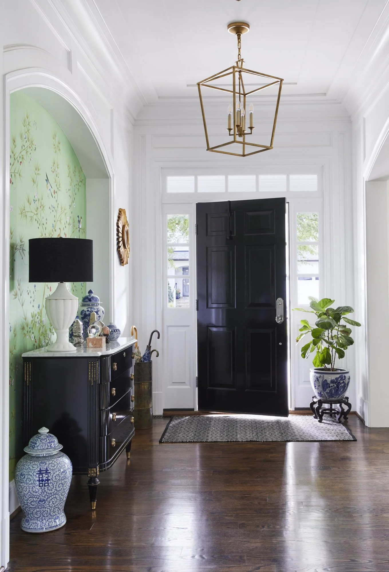 Chevy Chase entryway with a black front door, green accent wallpaper, black console table, decorative vases, and warm wood flooring.