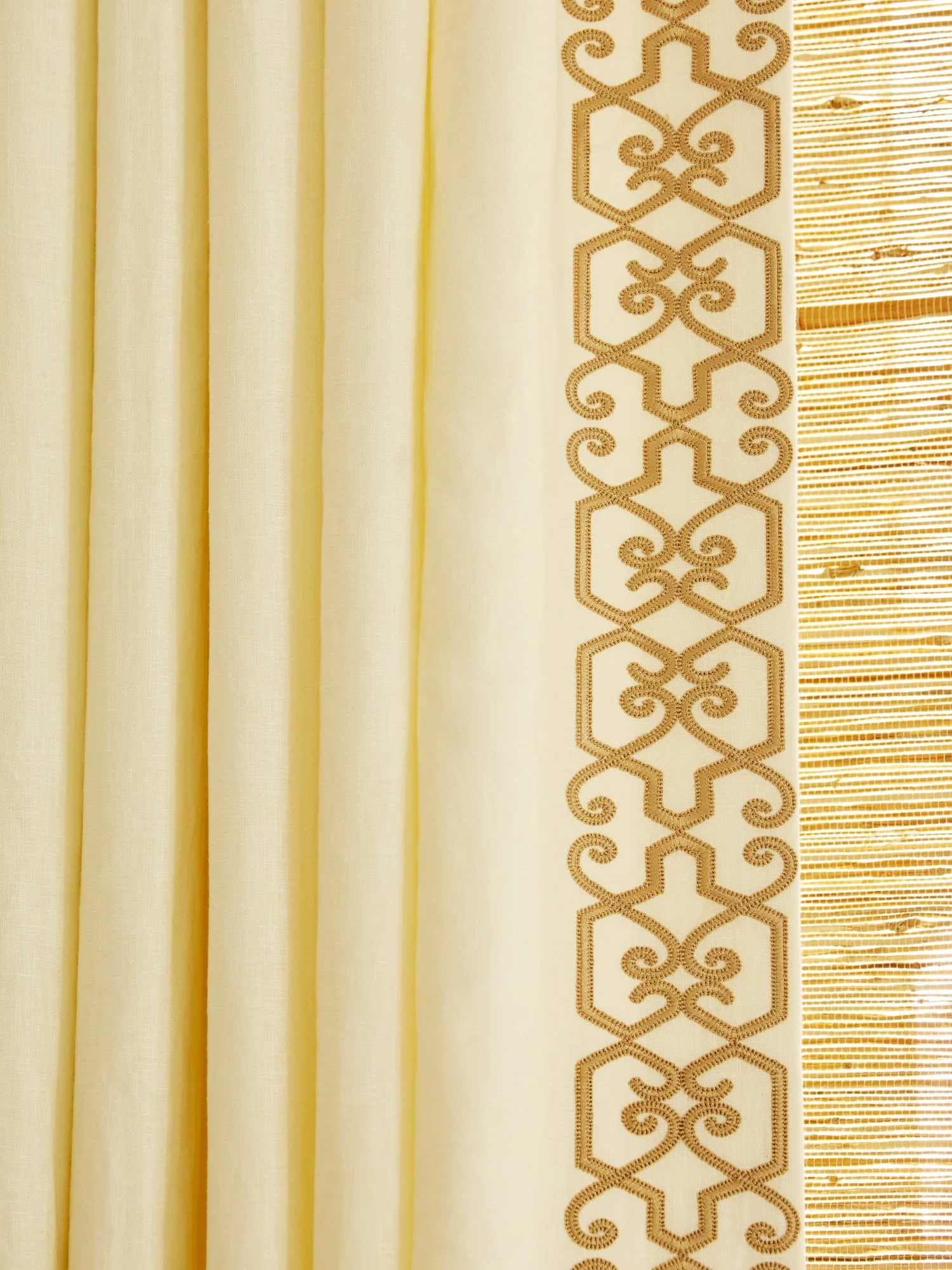 Close-up of a yellow curtain with embroidered geometric trim beside a woven bamboo shade.