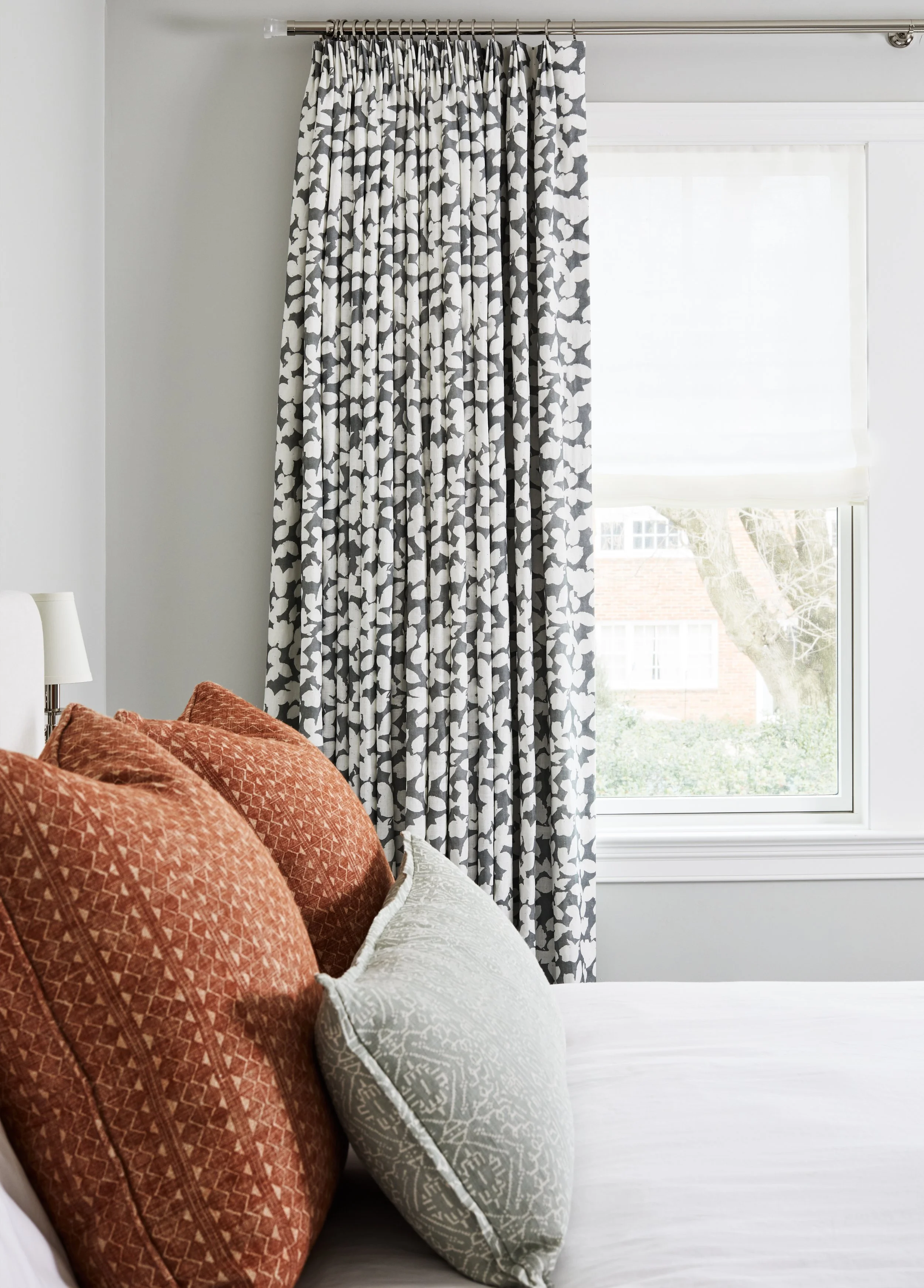 Bedroom with patterned window curtains and layered decorative pillows on the bed.