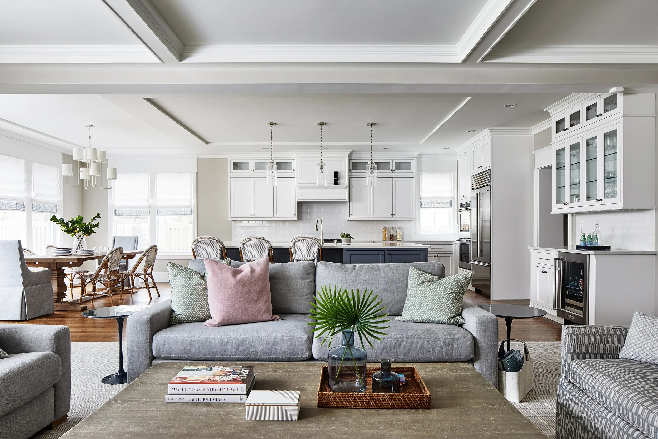 Open-concept Kensington home with gray sofas, pink and green pillows, a wood coffee table, dining area, and white kitchen.