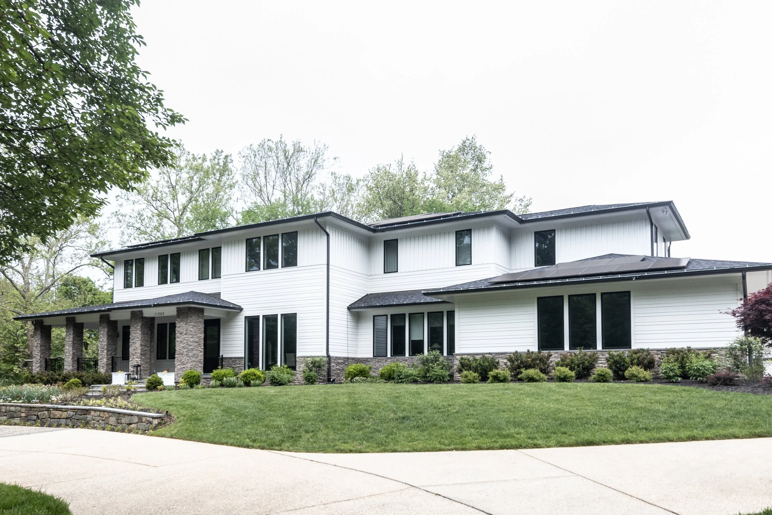 Large two-story Potomac home with a white exterior, stone accents, black roof, and surrounding greenery.