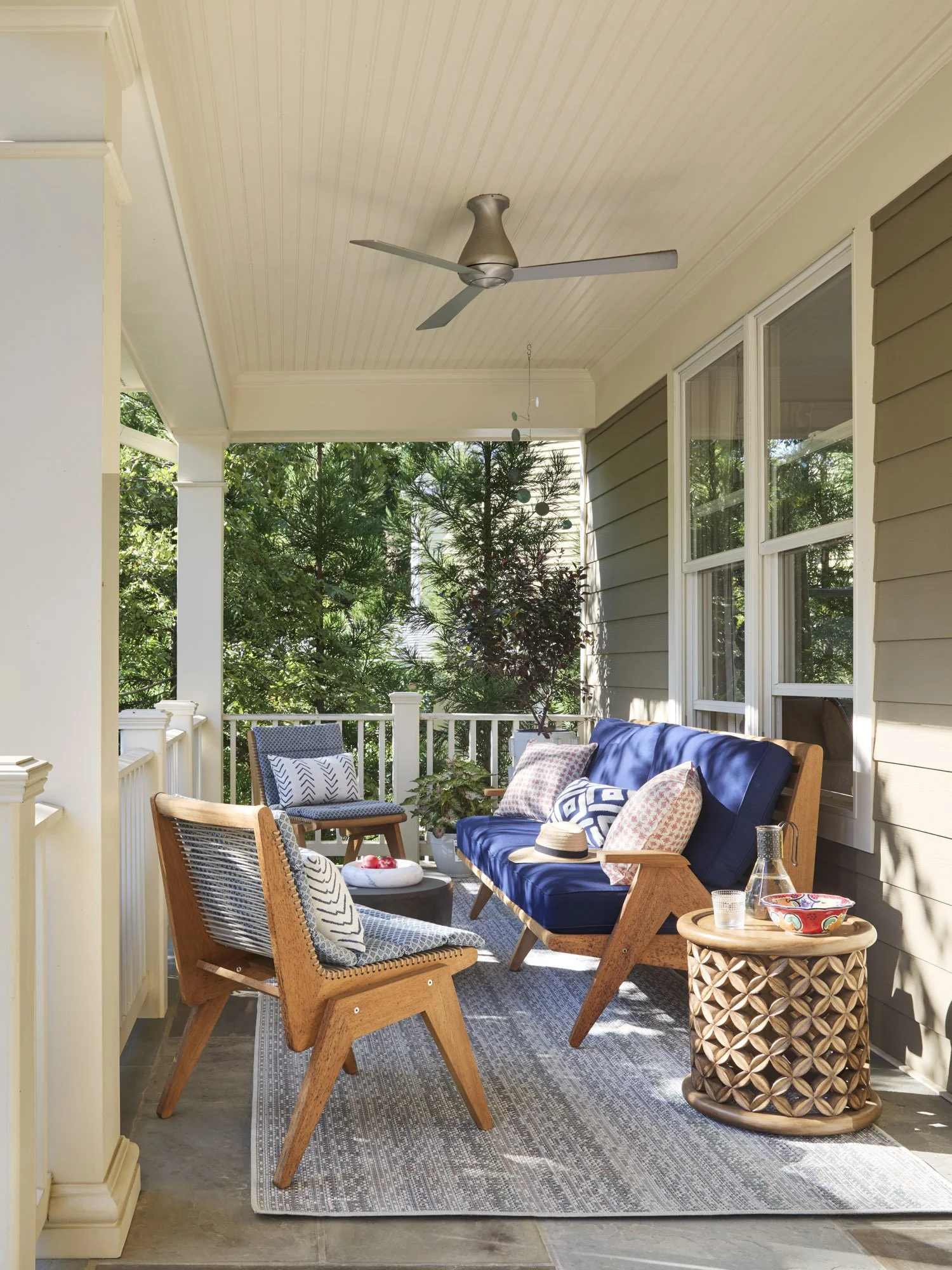 Covered patio with blue-cushioned seating, a patterned outdoor rug, ceiling fan, and surrounding garden.