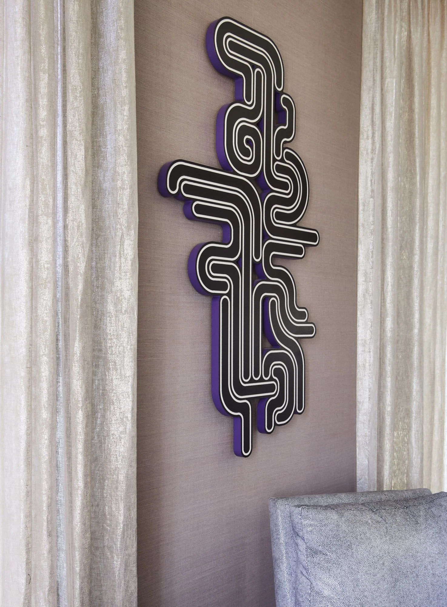 Black-and-white geometric artwork displayed beside shimmering curtains and a textured gray chair.