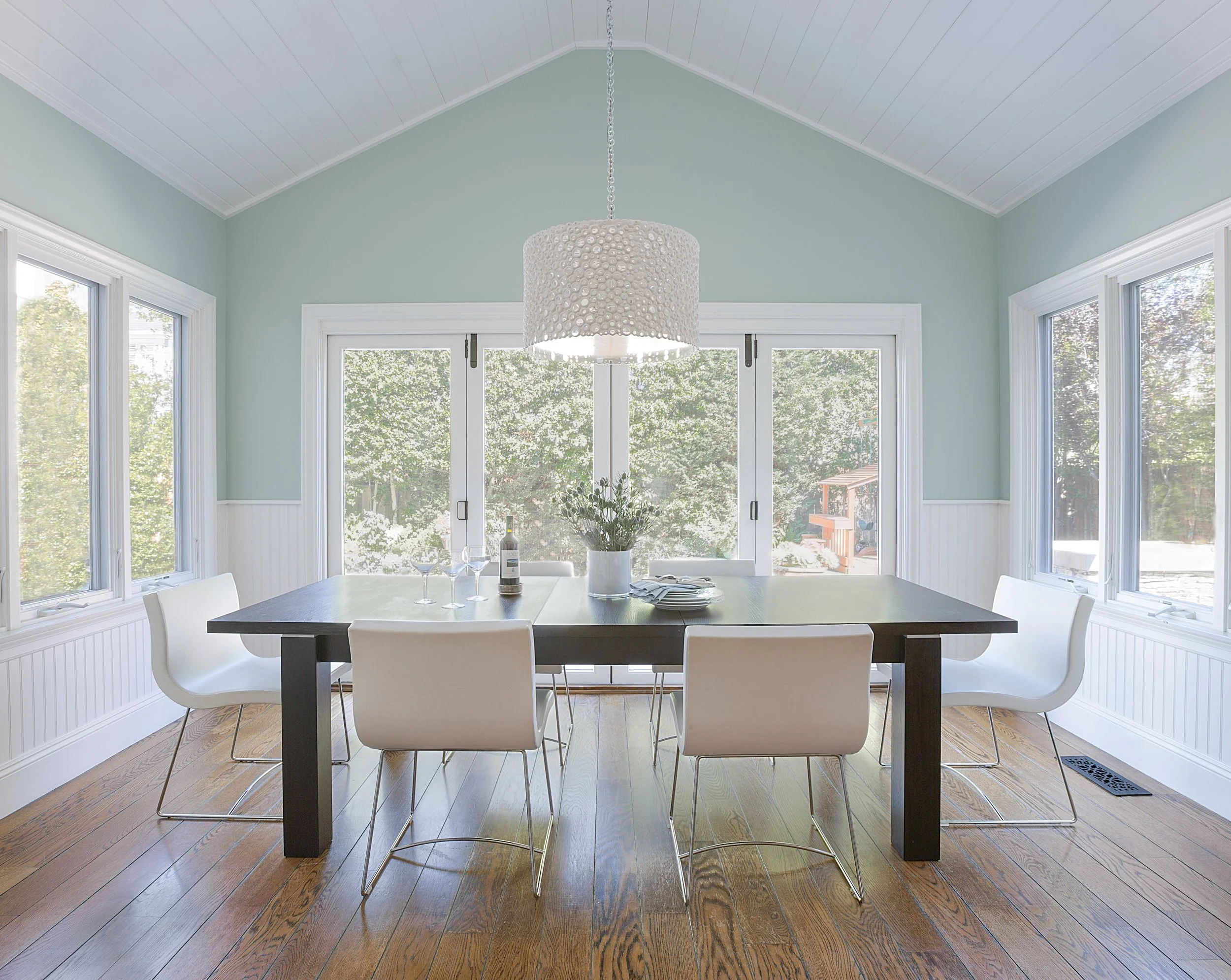 Contemporary dining room with a dark wood table, white chairs, mint green walls, modern pendant light, and sliding doors to the patio.