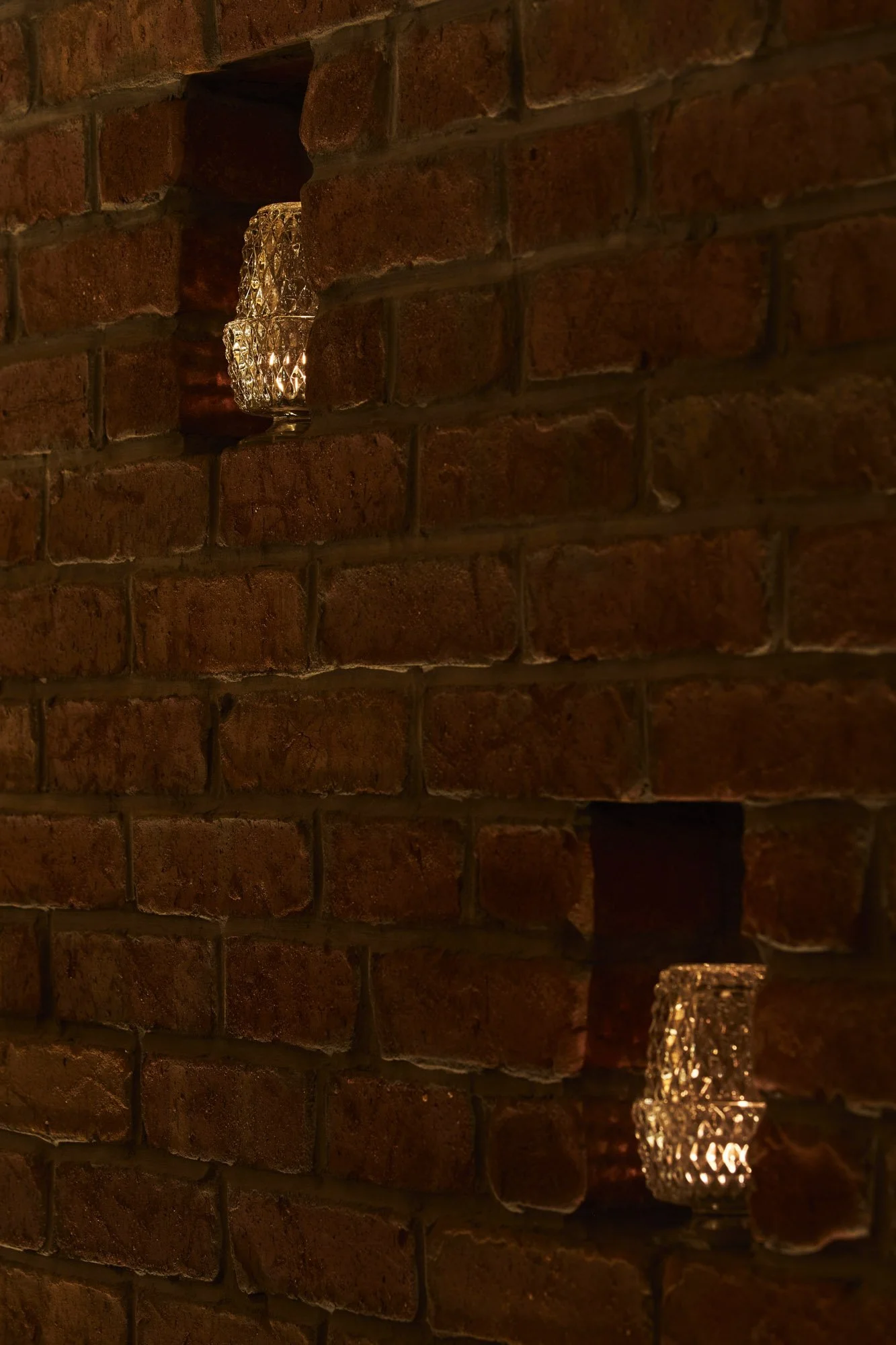 Small recessed niches with decorative glass lights set into the speakeasy’s brick wall.