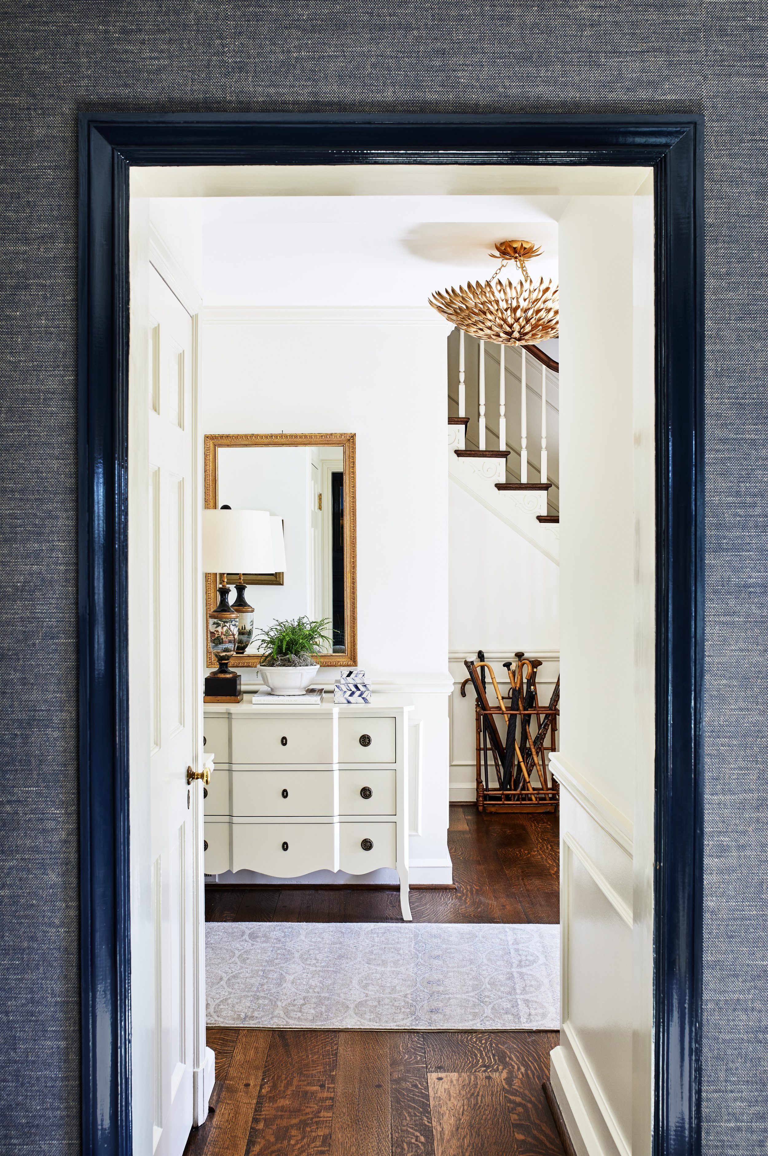 Traditional Kent, DC entryway with a white chest, brass mirror, table lamp, potted plant, dark wood flooring, and a staircase.