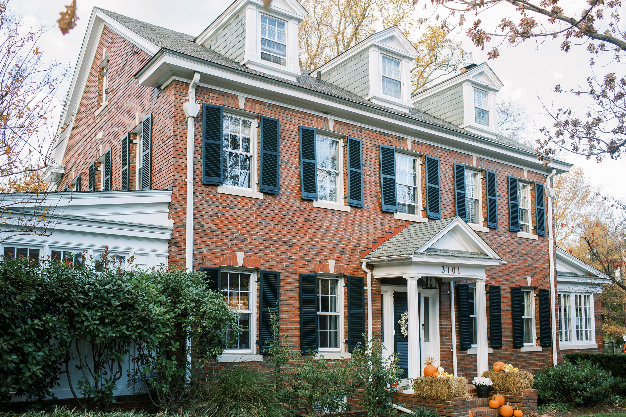 Two-story brick Colonial home in Chevy Chase with black shutters, white columns, and a seasonal porch display.