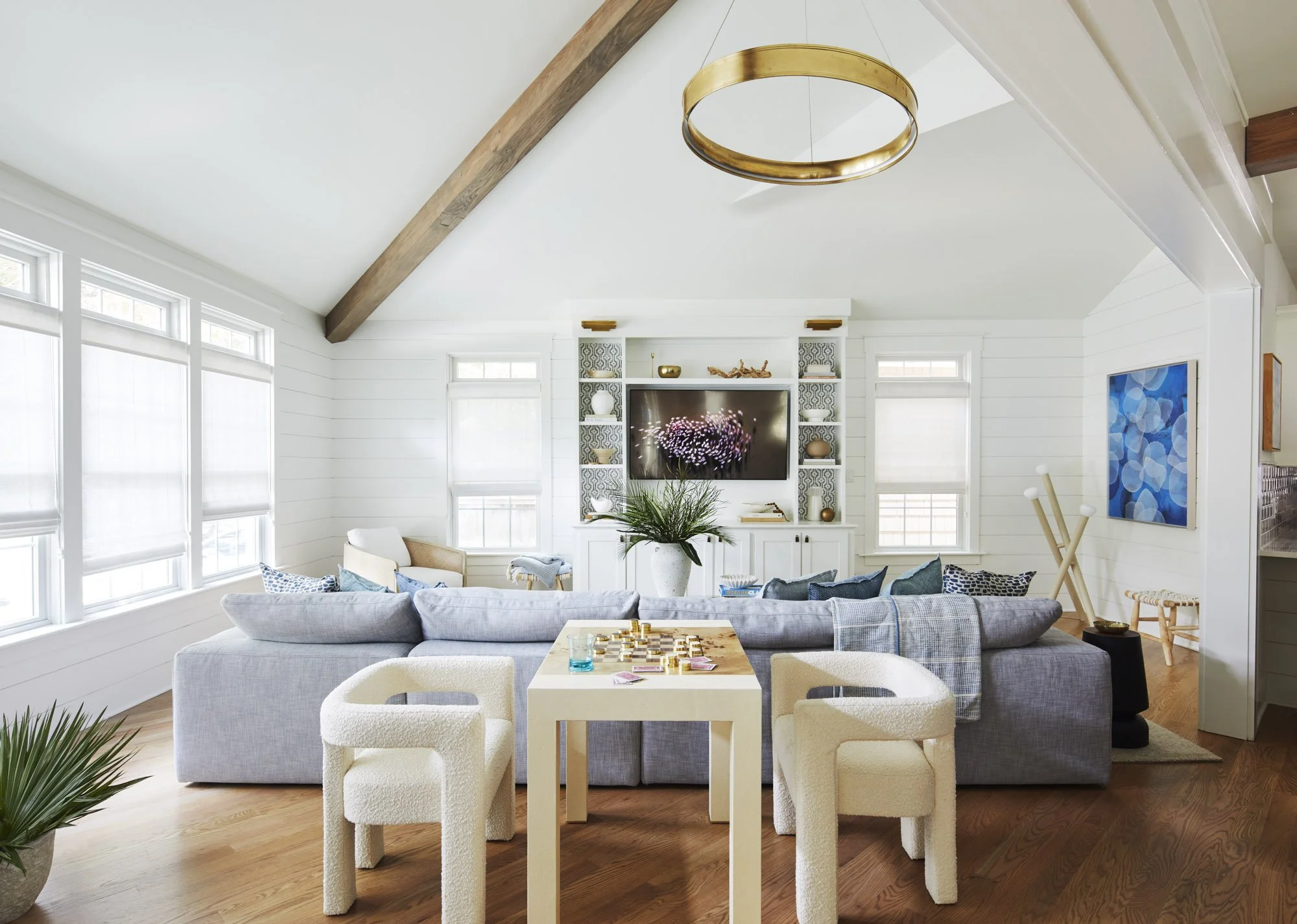 Gray sectional styled with blue pillows in a coastal living room with shiplap walls, a circular chandelier, and large windows.
