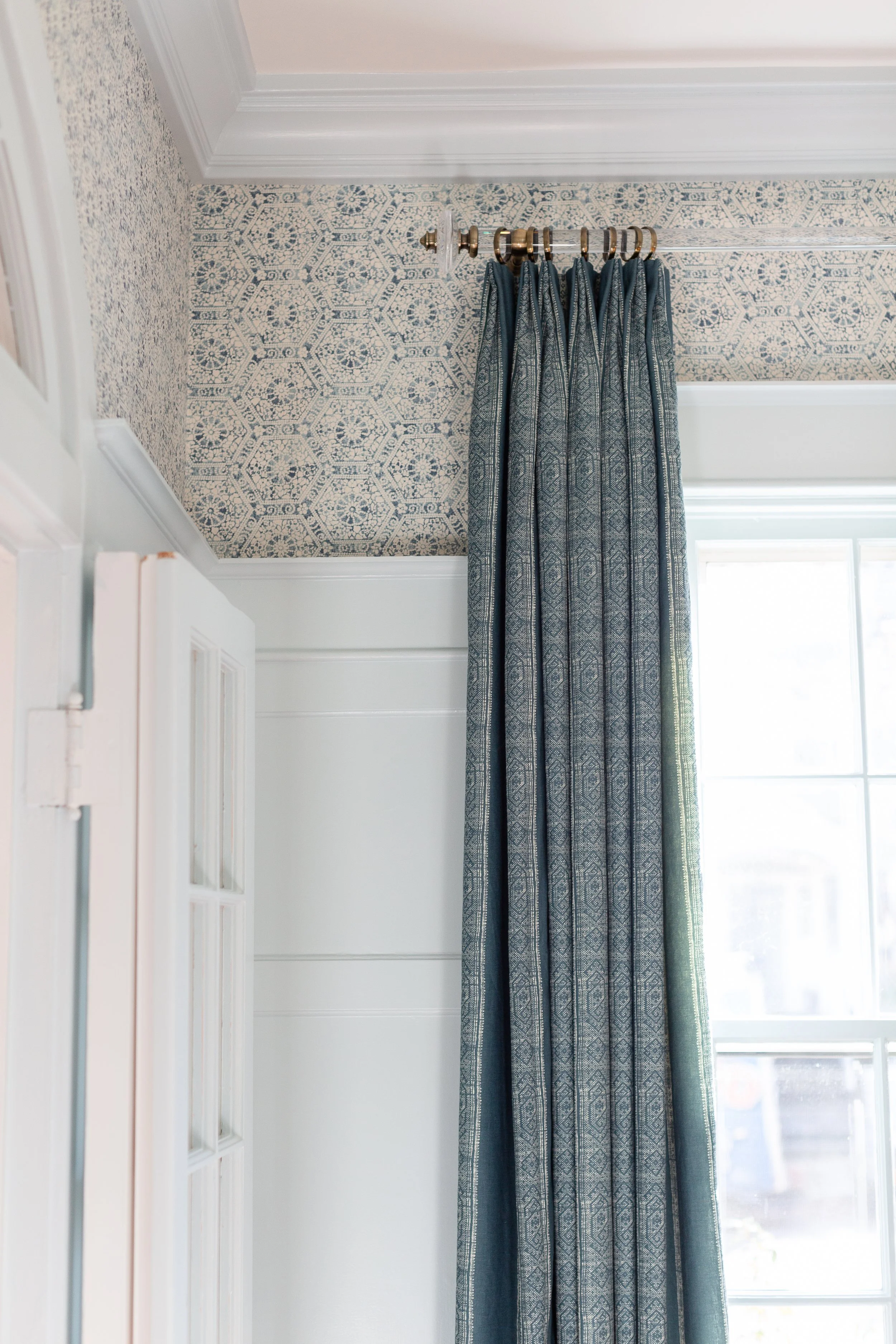 Patterned wallpaper and tailored blue curtains framing a bright dining room window.