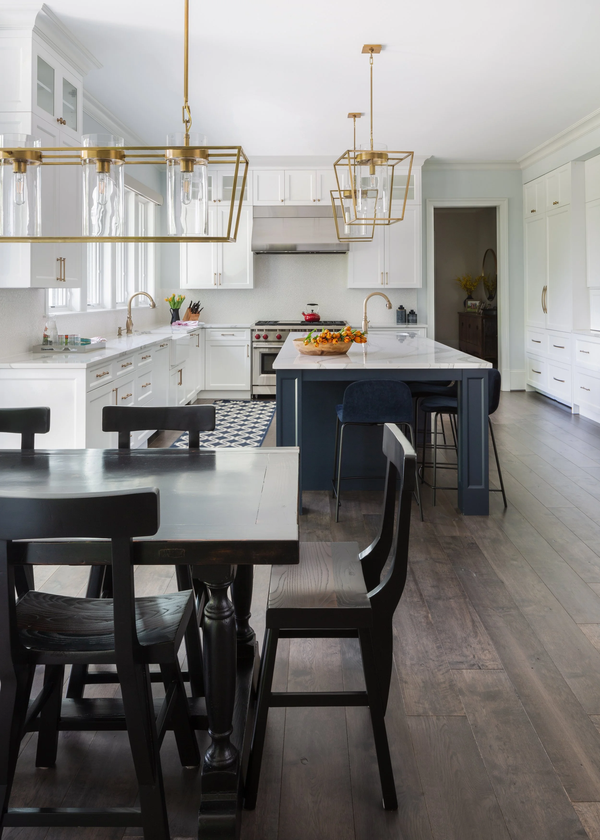 Open kitchen and dining area with white cabinetry, a dark wood table, upholstered chairs, and brass pendant lights.
