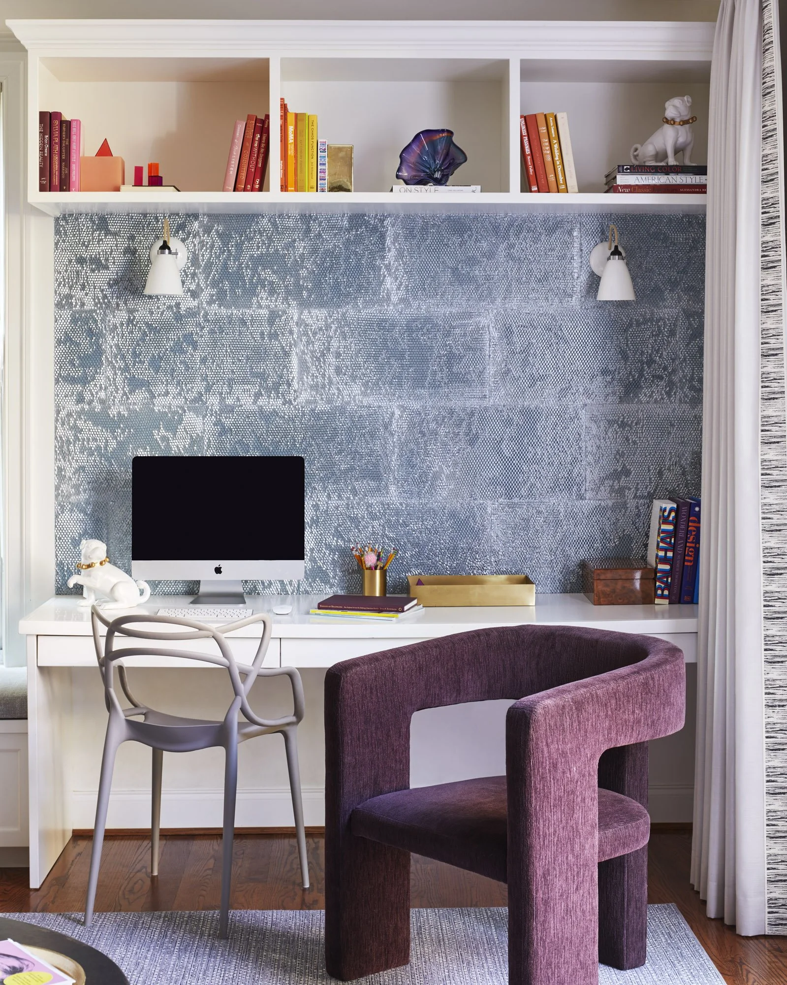 Compact home office with a streamlined desk, computer, dog sculpture, task lamp, colorful books, and two contemporary chairs.