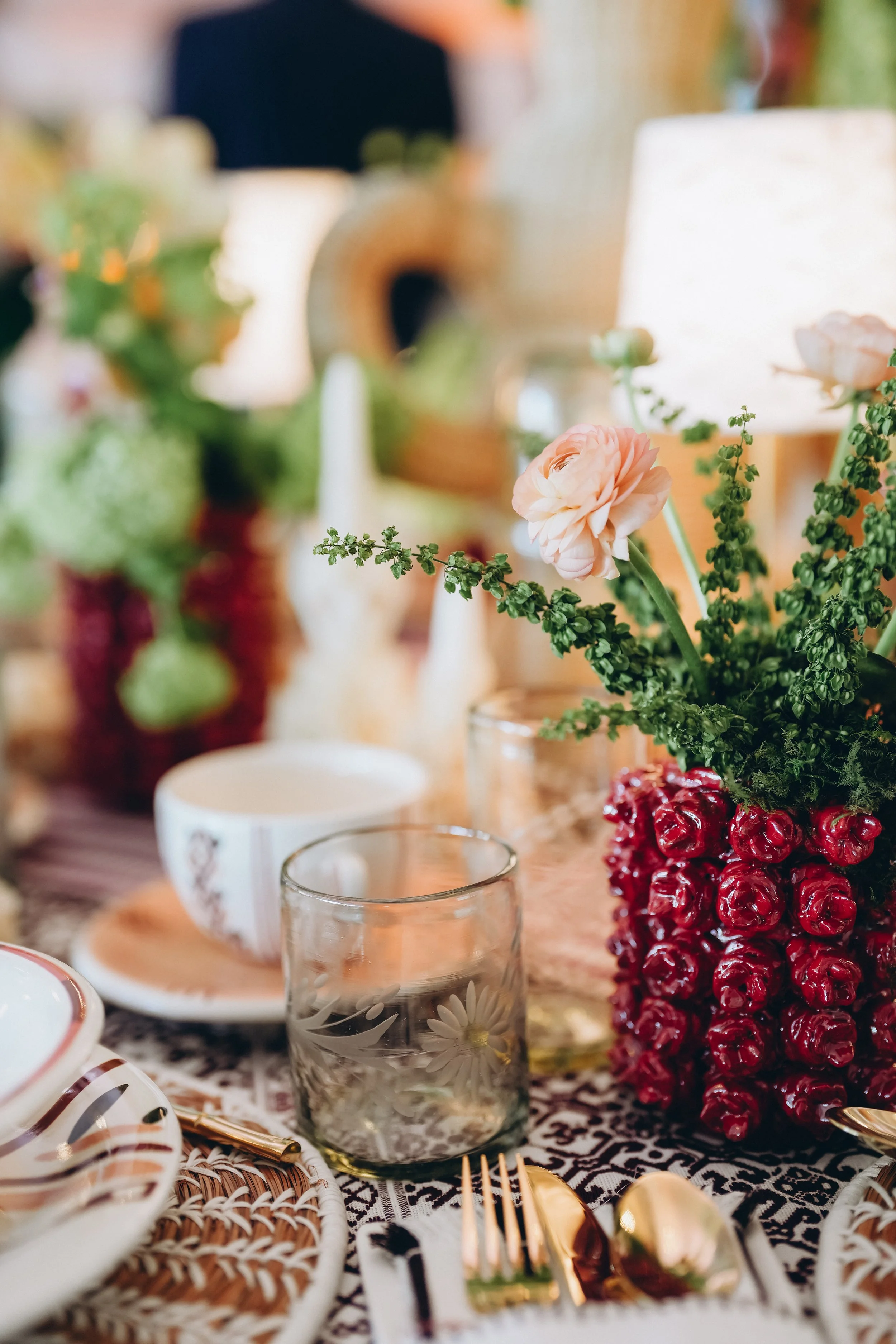 Naples Tables place setting with handmade ceramics, woven chargers, gold flatware, etched glassware, and colorful flowers.