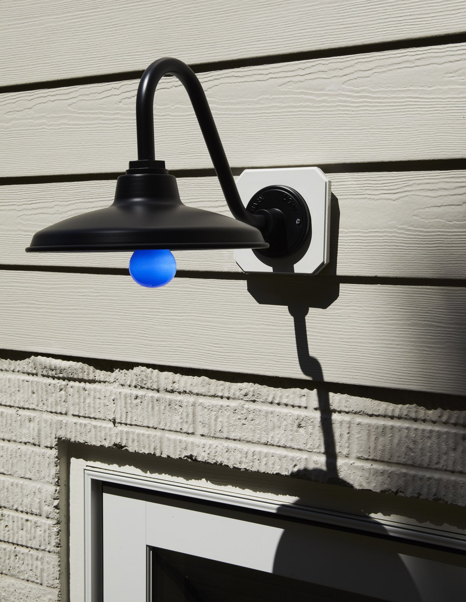 Vintage black wall-mounted light with a blue bulb installed above a window on a pale green wall.