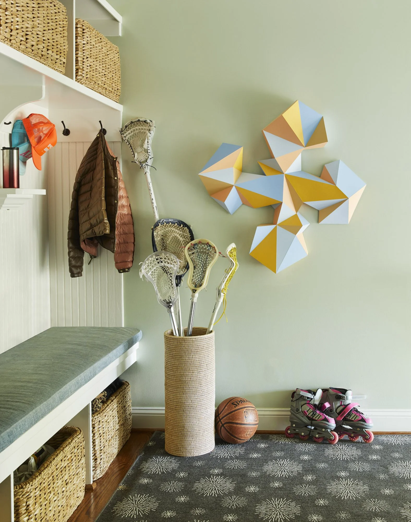 Family mudroom with a storage bench, woven baskets, coat hooks, lacrosse sticks, rollerblades, and a basketball.