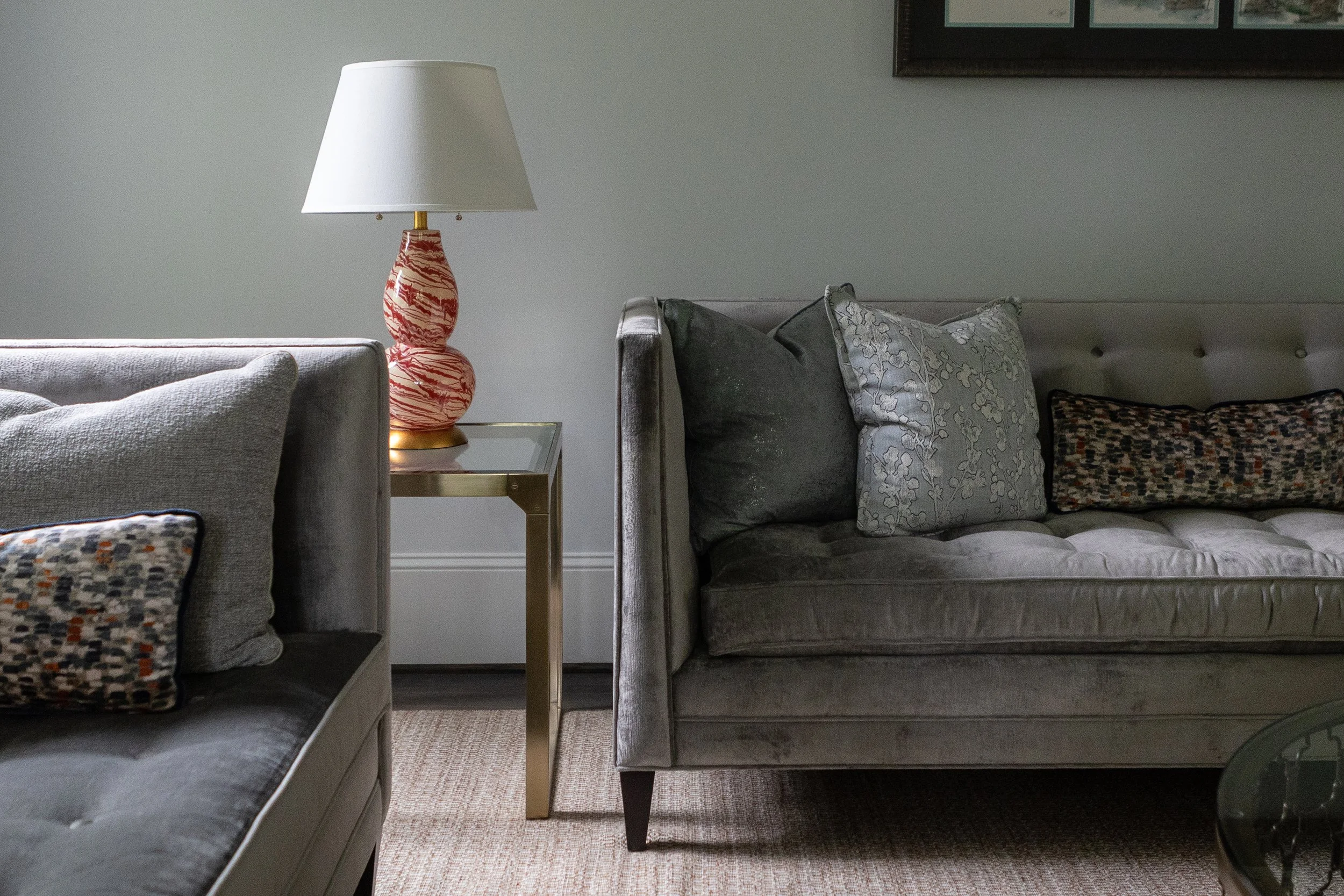 Gray sofas with patterned pillows beside a glass-topped table, red-and-white swirl lamp, and framed artwork.