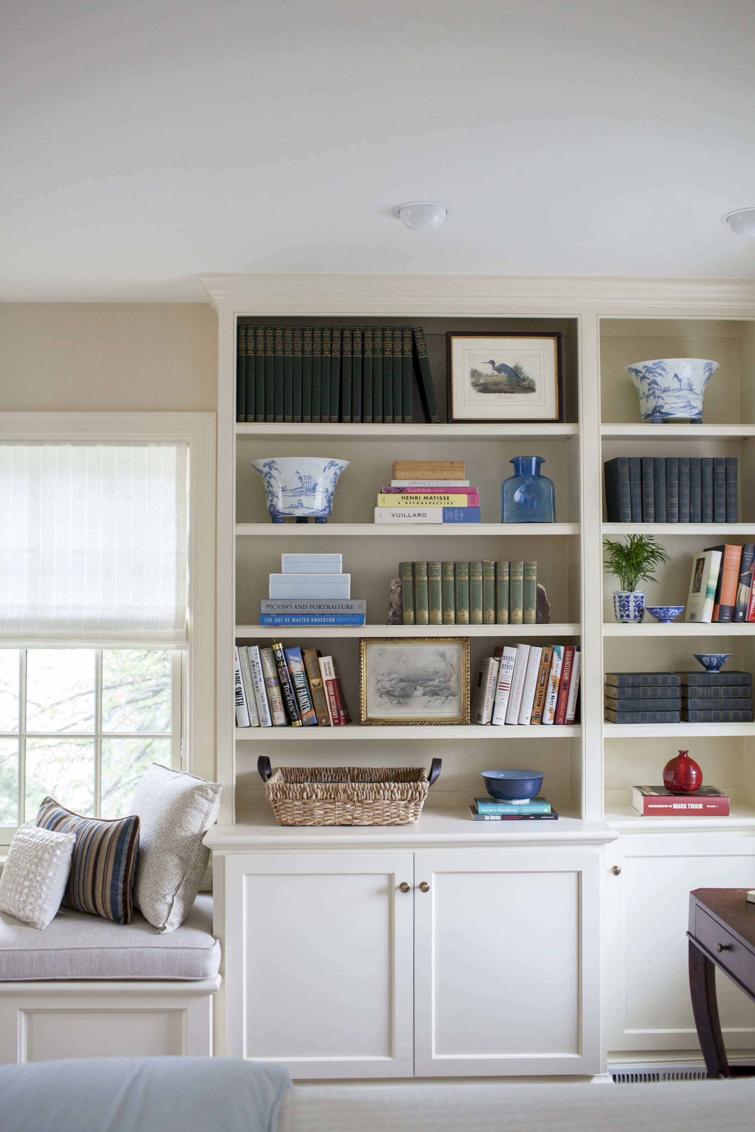 Built-in bedroom bookshelf styled with books, decorative objects, and a woven basket beside a cushioned bench.