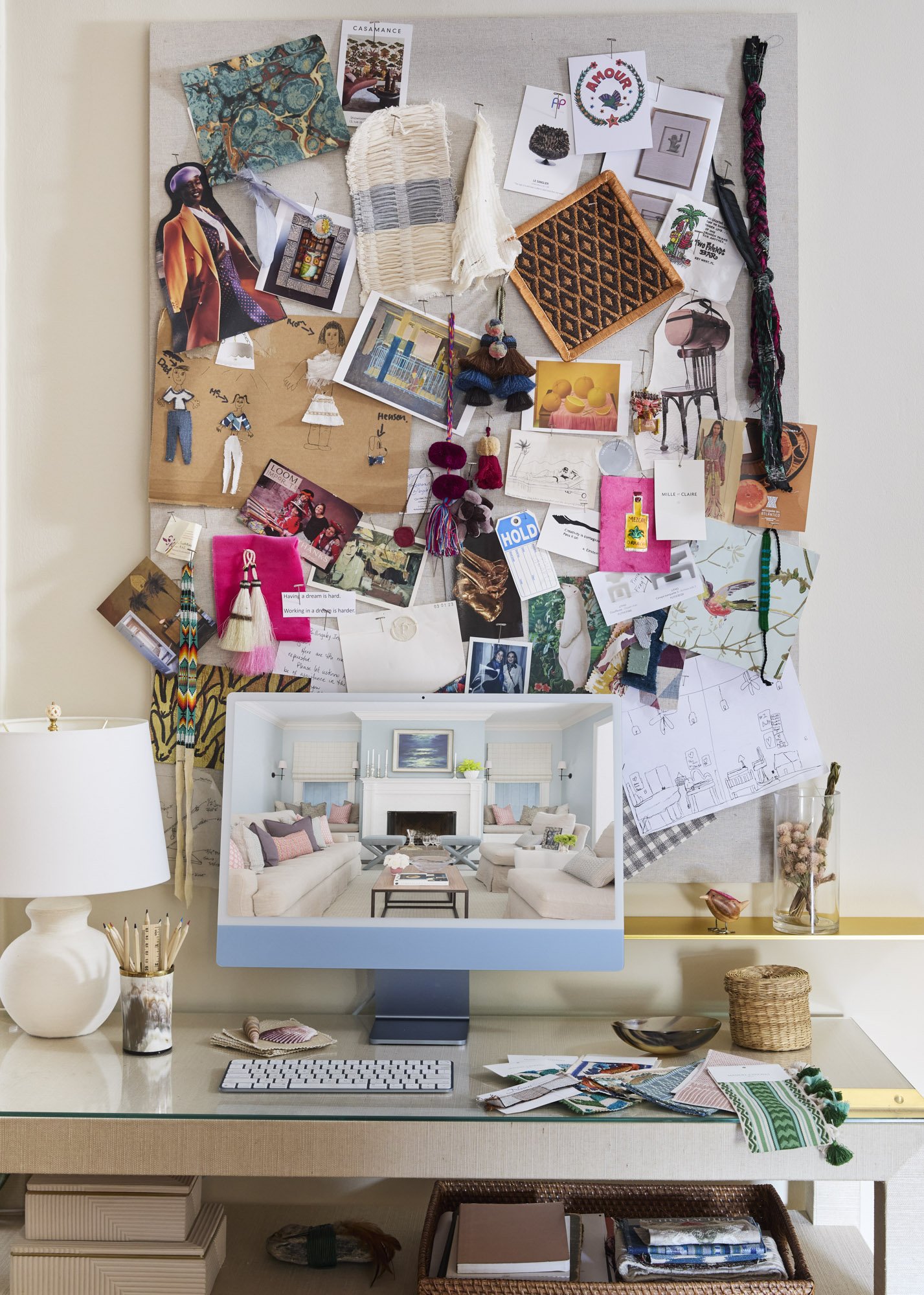 Interior design workspace with fabric samples, sketches, an inspiration board, and a computer displaying a finished living room.