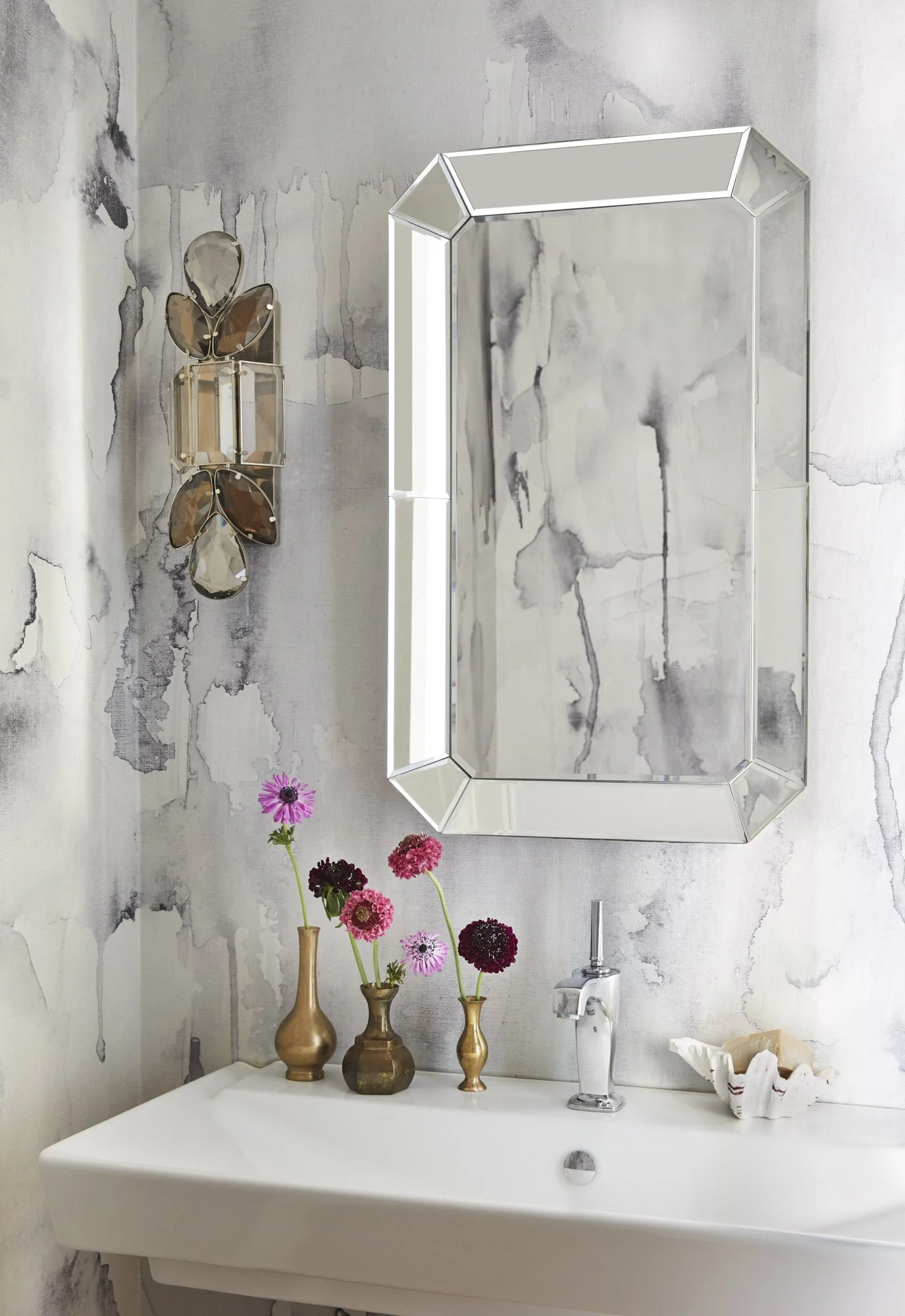 Powder room with watercolor-style wallpaper, an octagonal mirror, modern wall light, flowers, and decorative vessels.